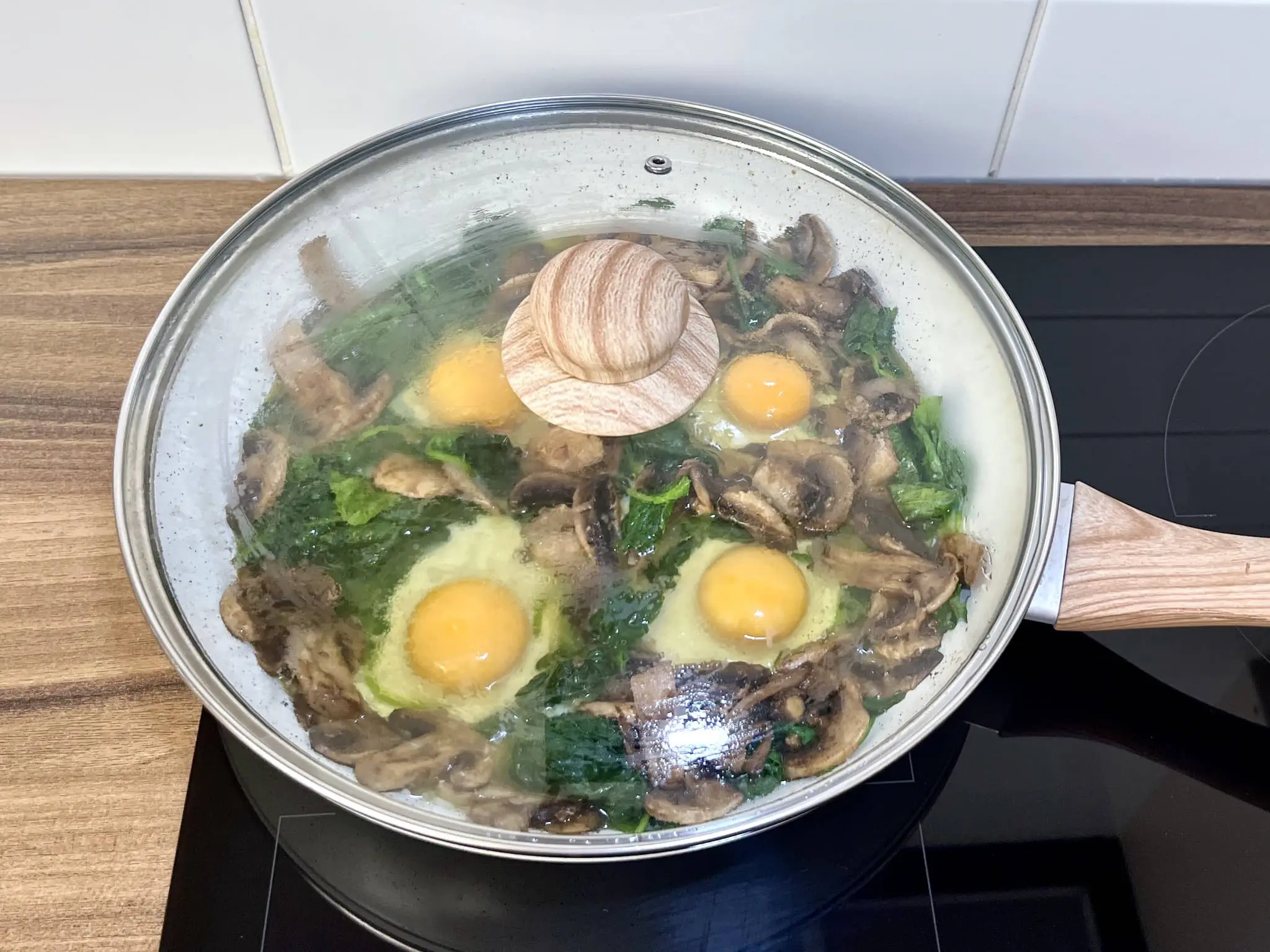 Eggs cooking with spinach and mushrooms in a pan covered with a lid