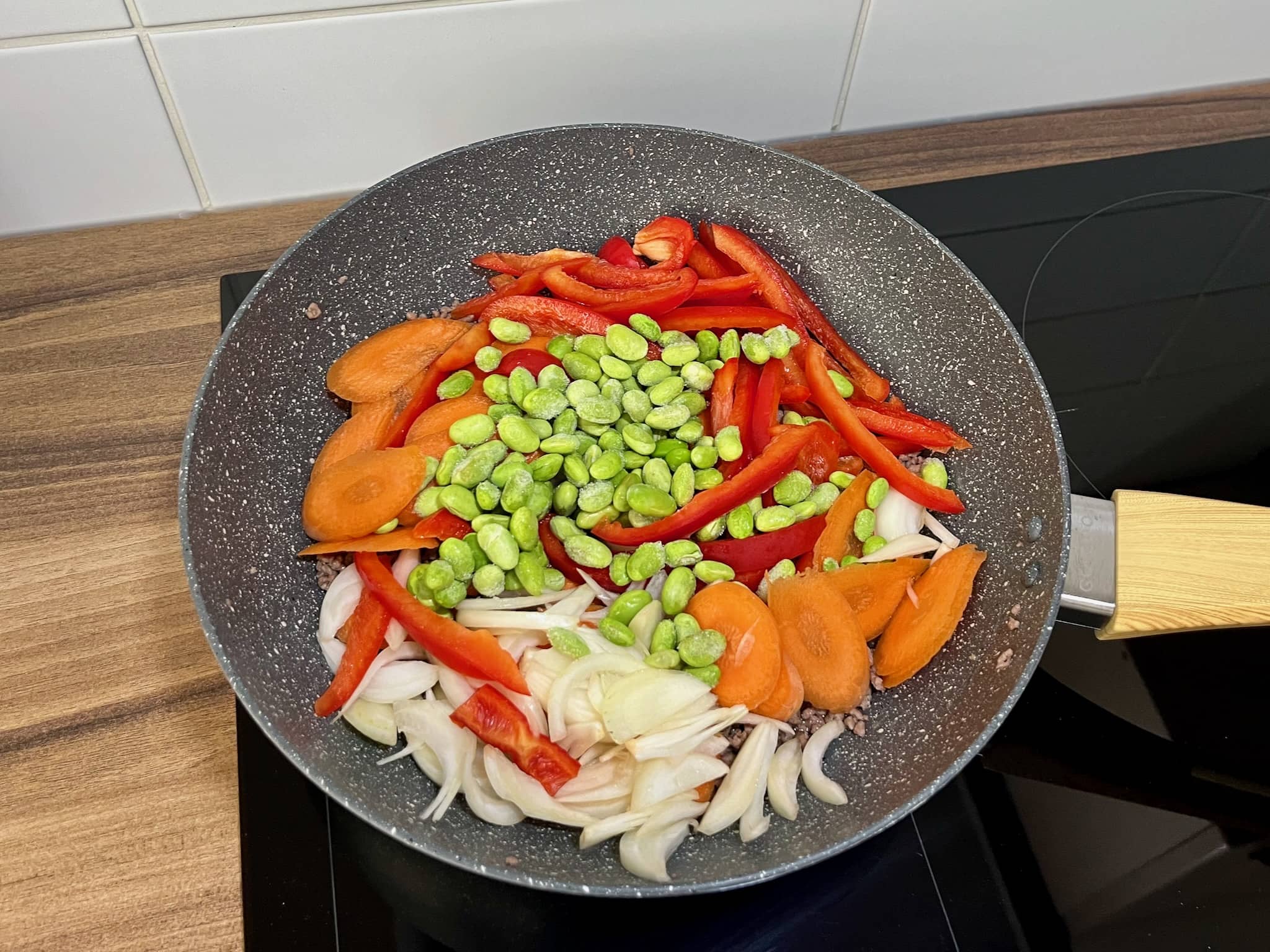 Vegetables and soybeans are added to the beef in the pan