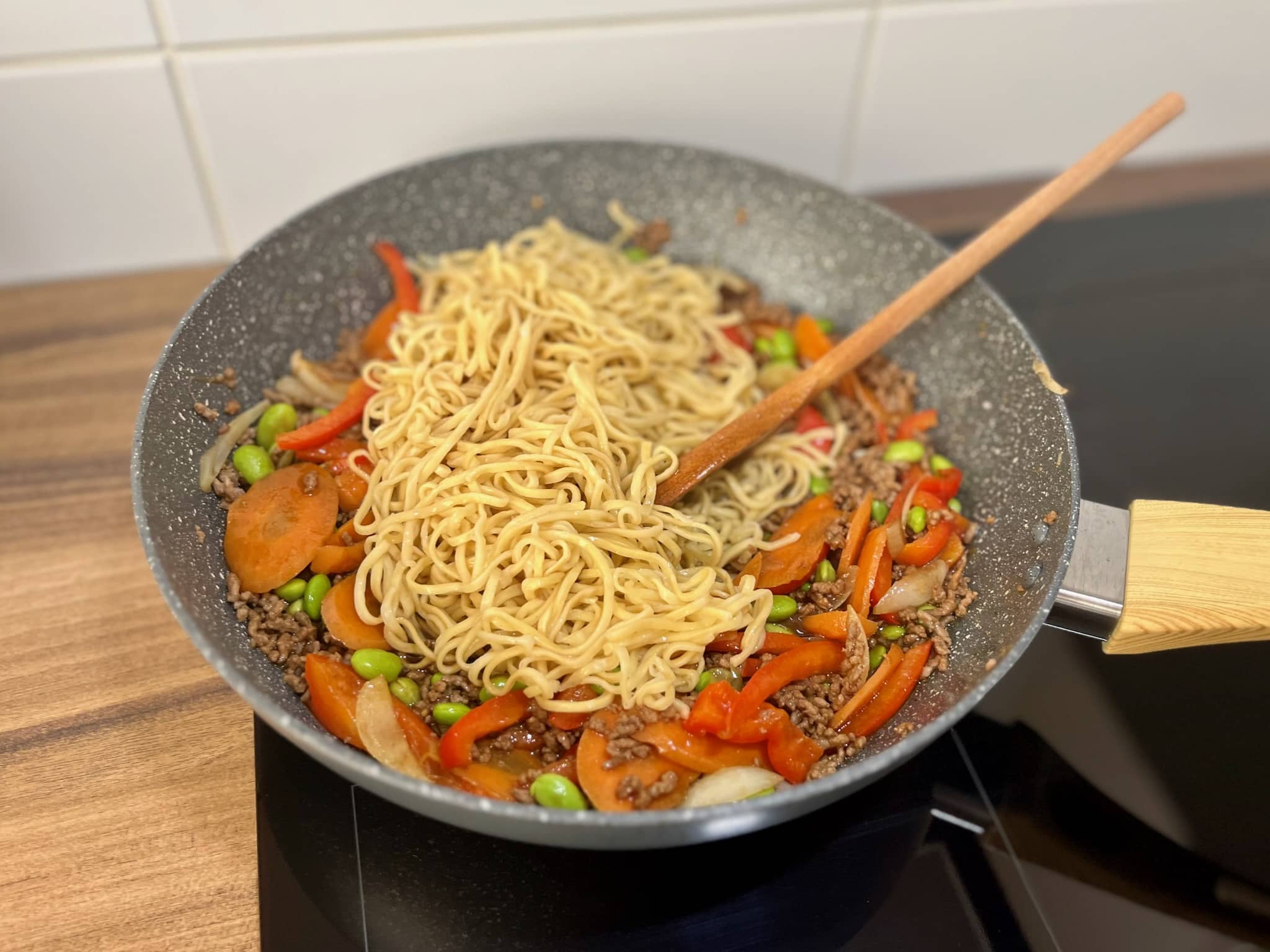Cooked egg noodles are added to the vegetables and ground beef in the pan