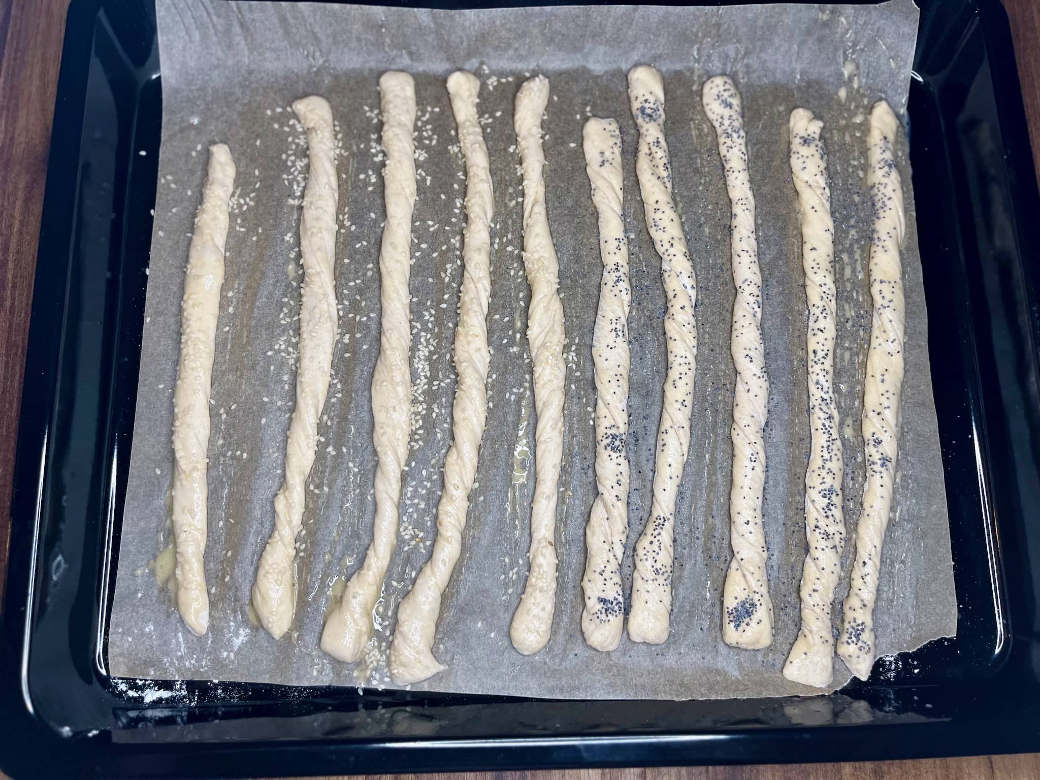 Breadsticks dough egg washed and sprinkled with sesame and poppy seeds on the baking tray ready for baking