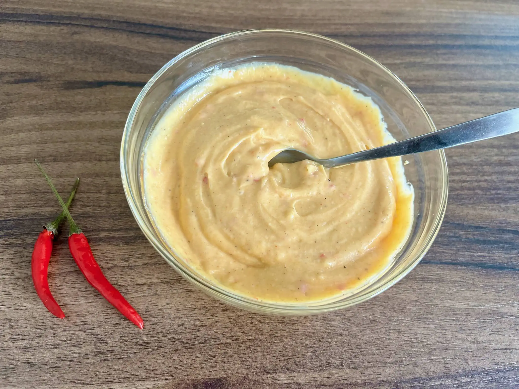Domowy pikantny majonez w misce z dwiema papryczkami chilli obok