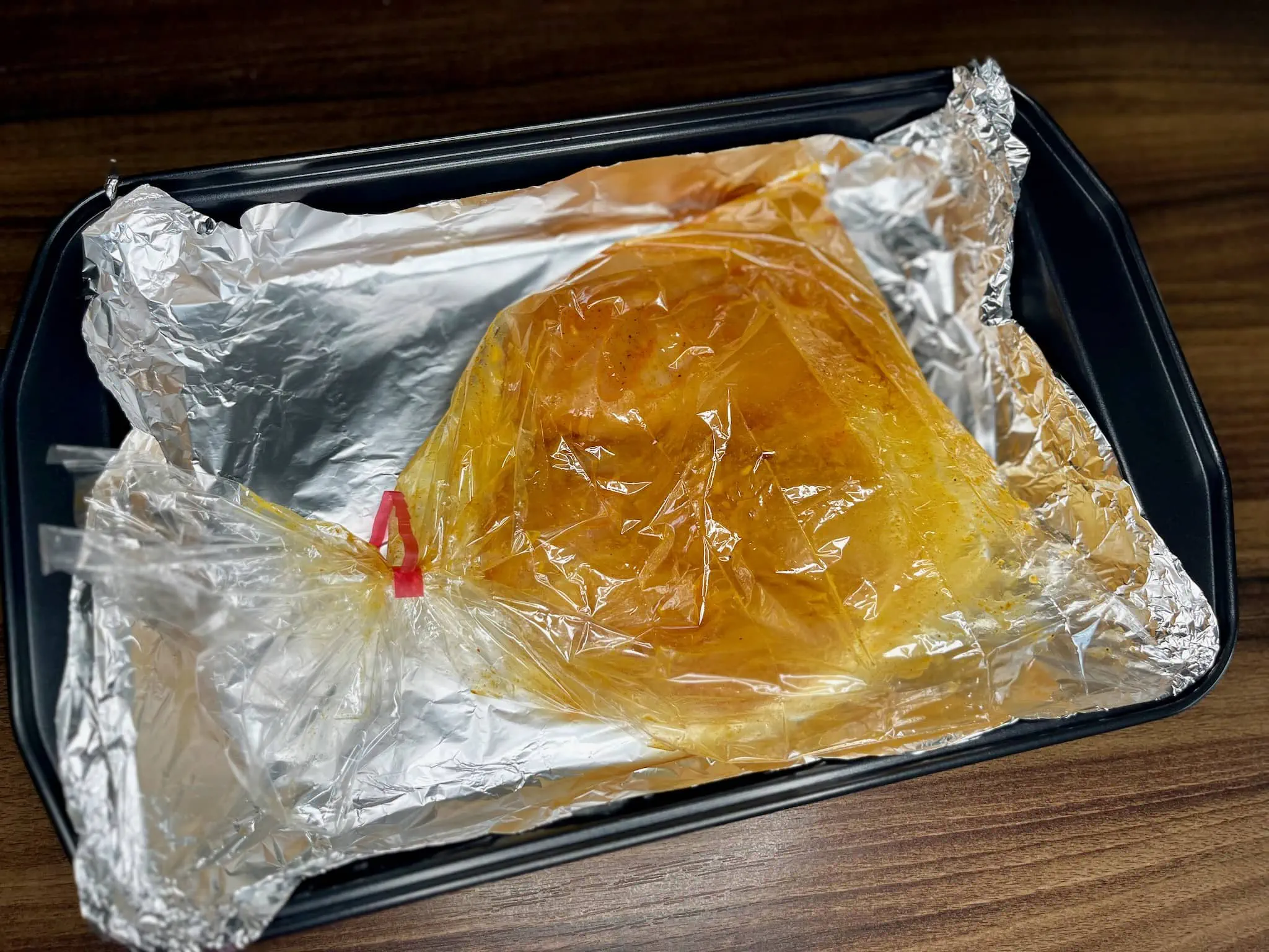Marinated chicken breasts are placed in a baking bag and set on a baking tray lined with aluminium foil