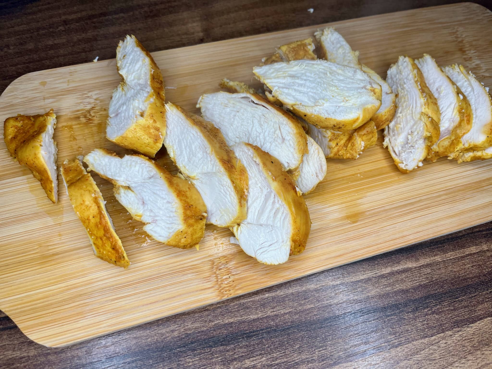 Tender, cooked chicken breasts are sliced on a cutting board