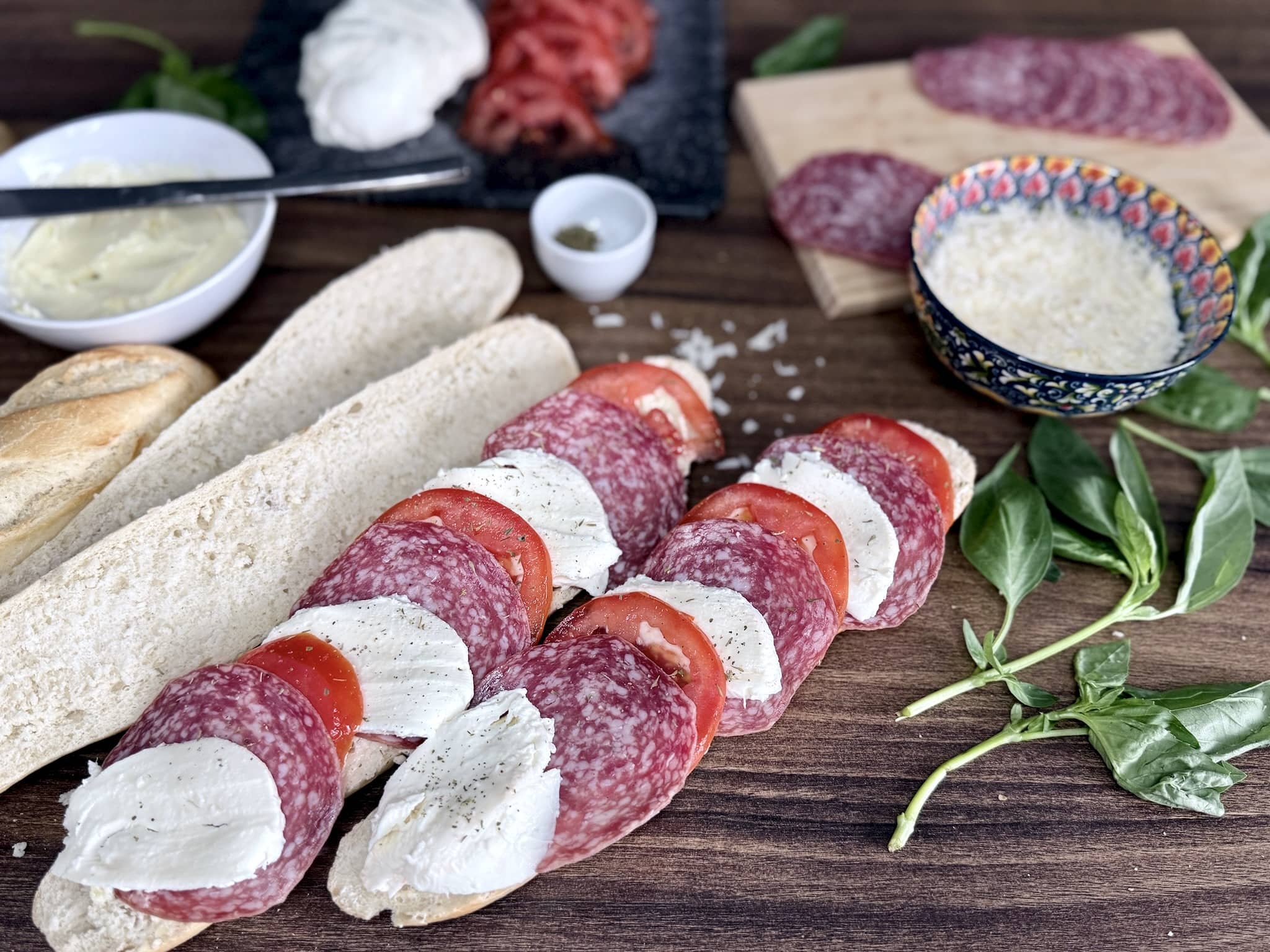 Baguettes being layered with salami, tomatoes, and mozzarella