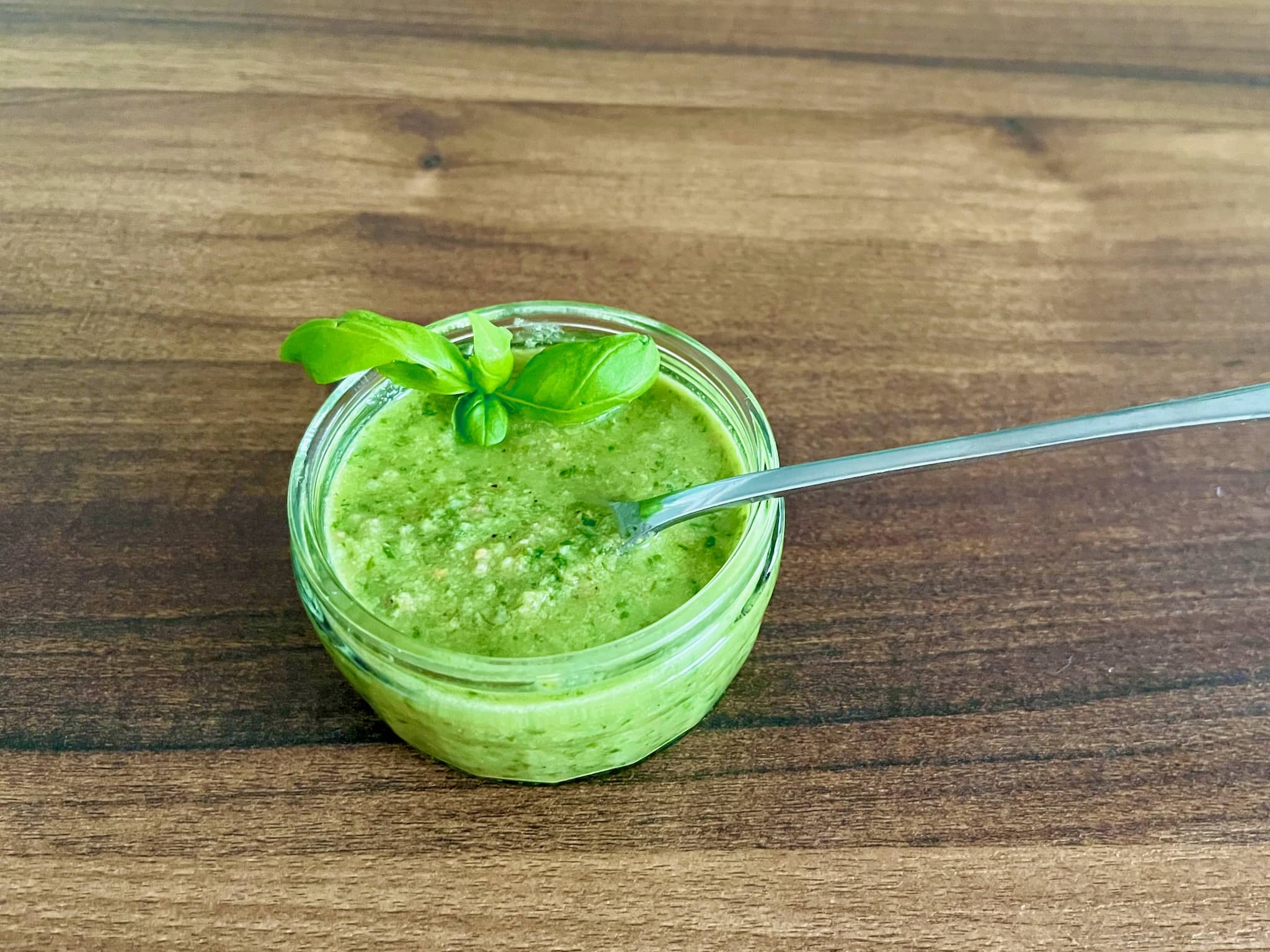 Basil Pesto in a sauce glass with a spoon inside decorated with a fresh basil leaf