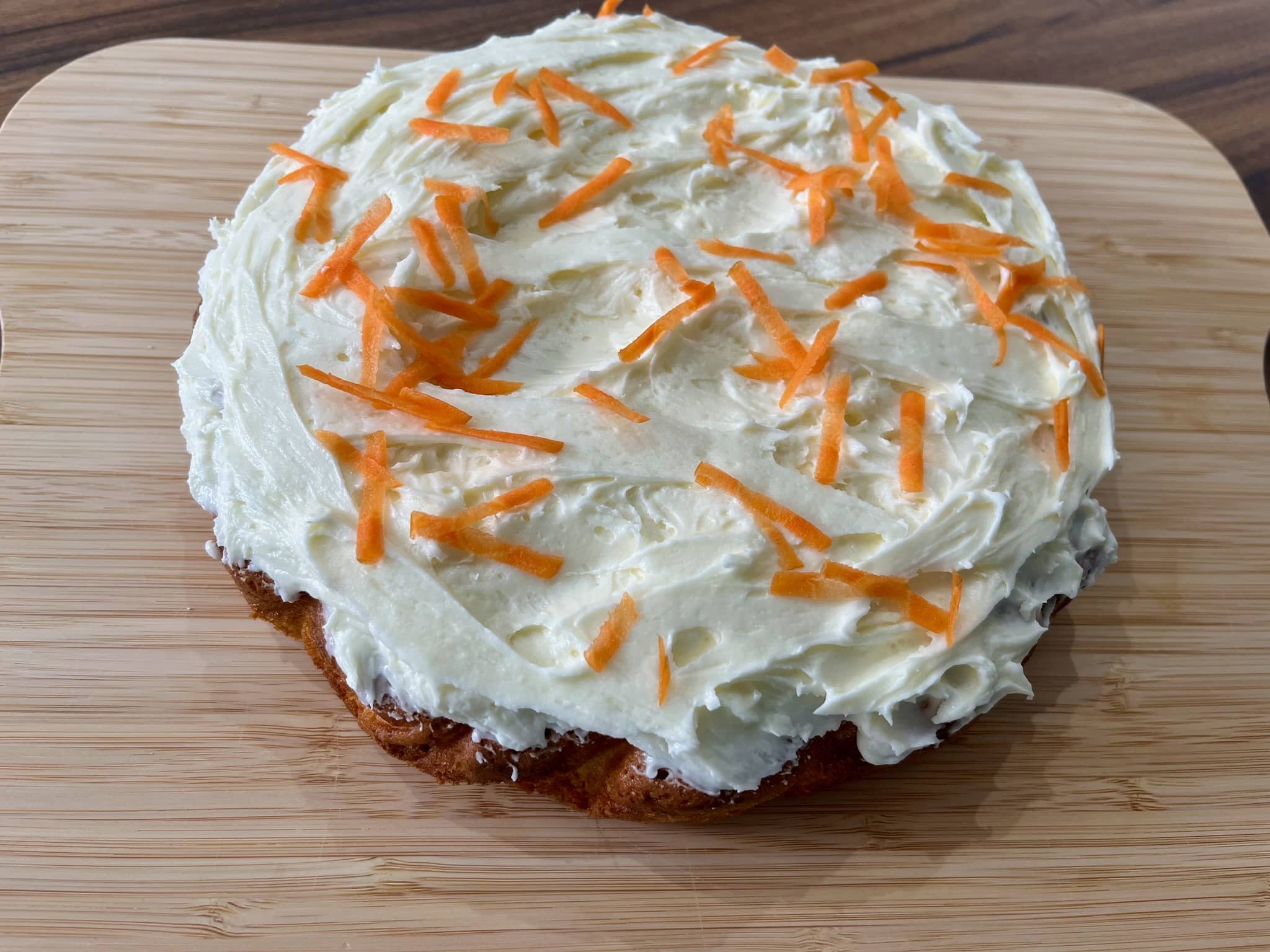 The baked carrot cake is decorated with icing and carrot shavings