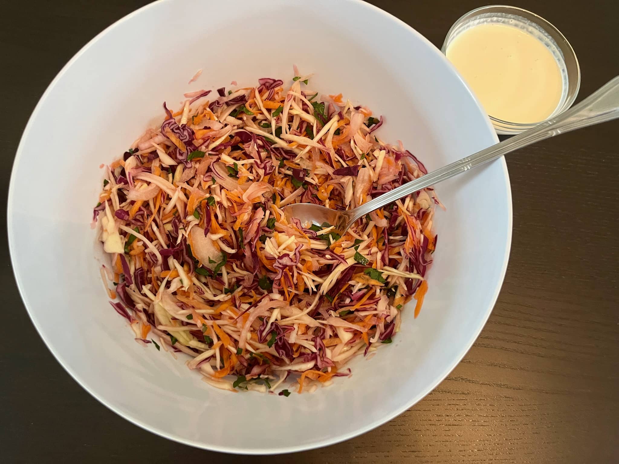 Raw coleslaw in a bowl with coleslaw dressing on a side