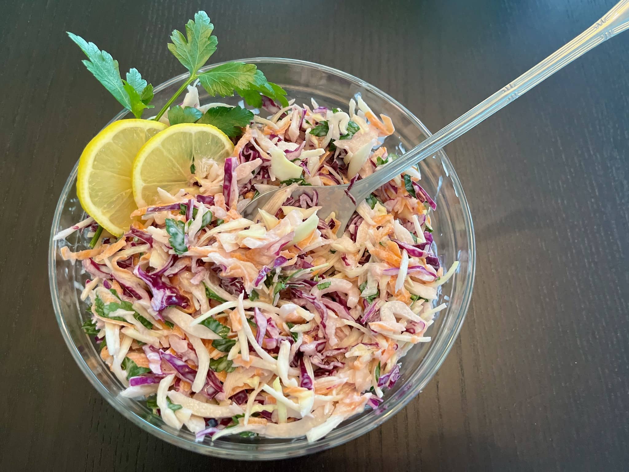 Simple Coleslaw in a bowl, decorated with slices of lemon and fresh parsley