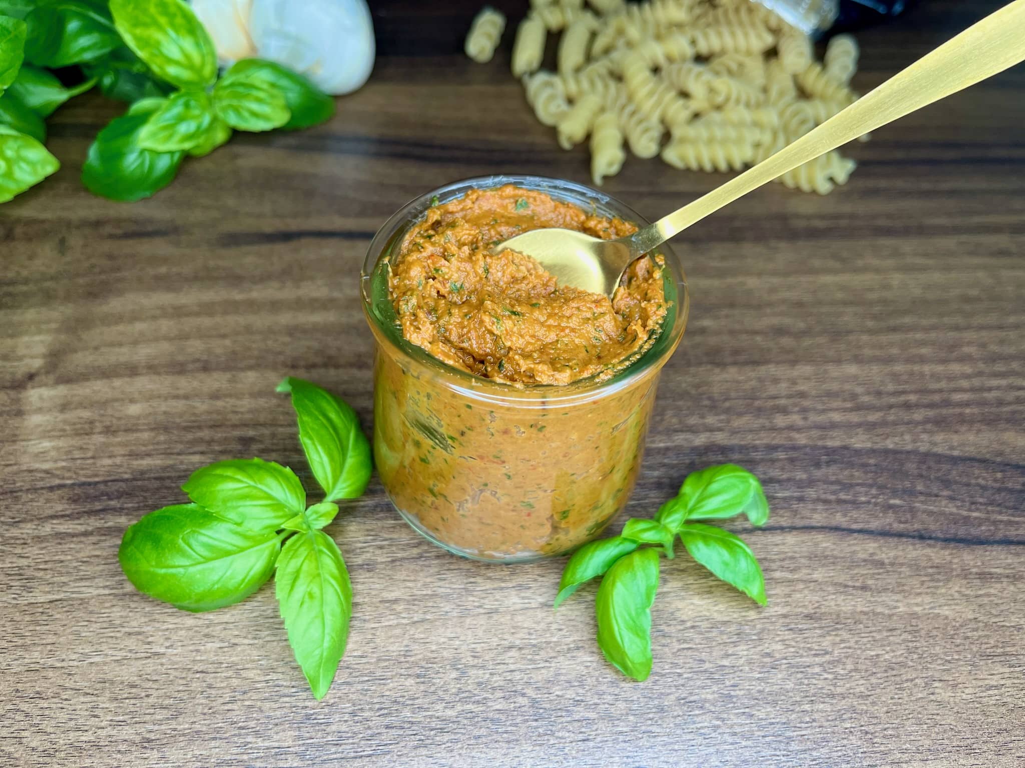 Red pesto in a jug, with basil leaves on the side