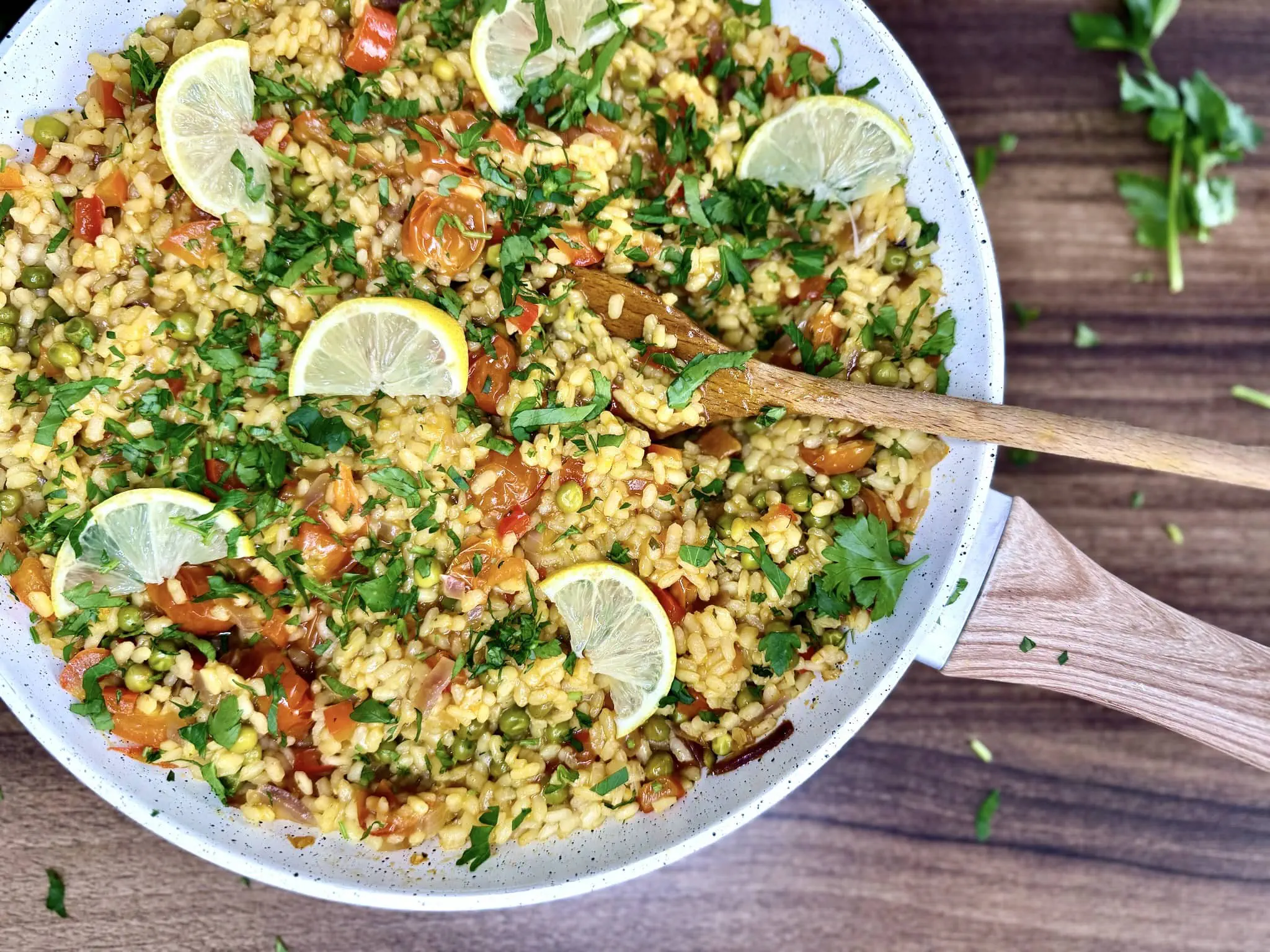 Świetnie przygotowana warzywna paella, udekorowana pietruszką i plasterkami cytryny, nadal na patelni