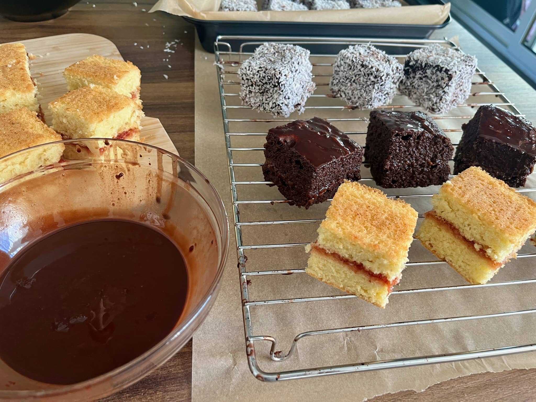 Plain sponge squares, squares coated in chocolate and suares coated in desiccated coconut on a tryl in process of making Lamingtons