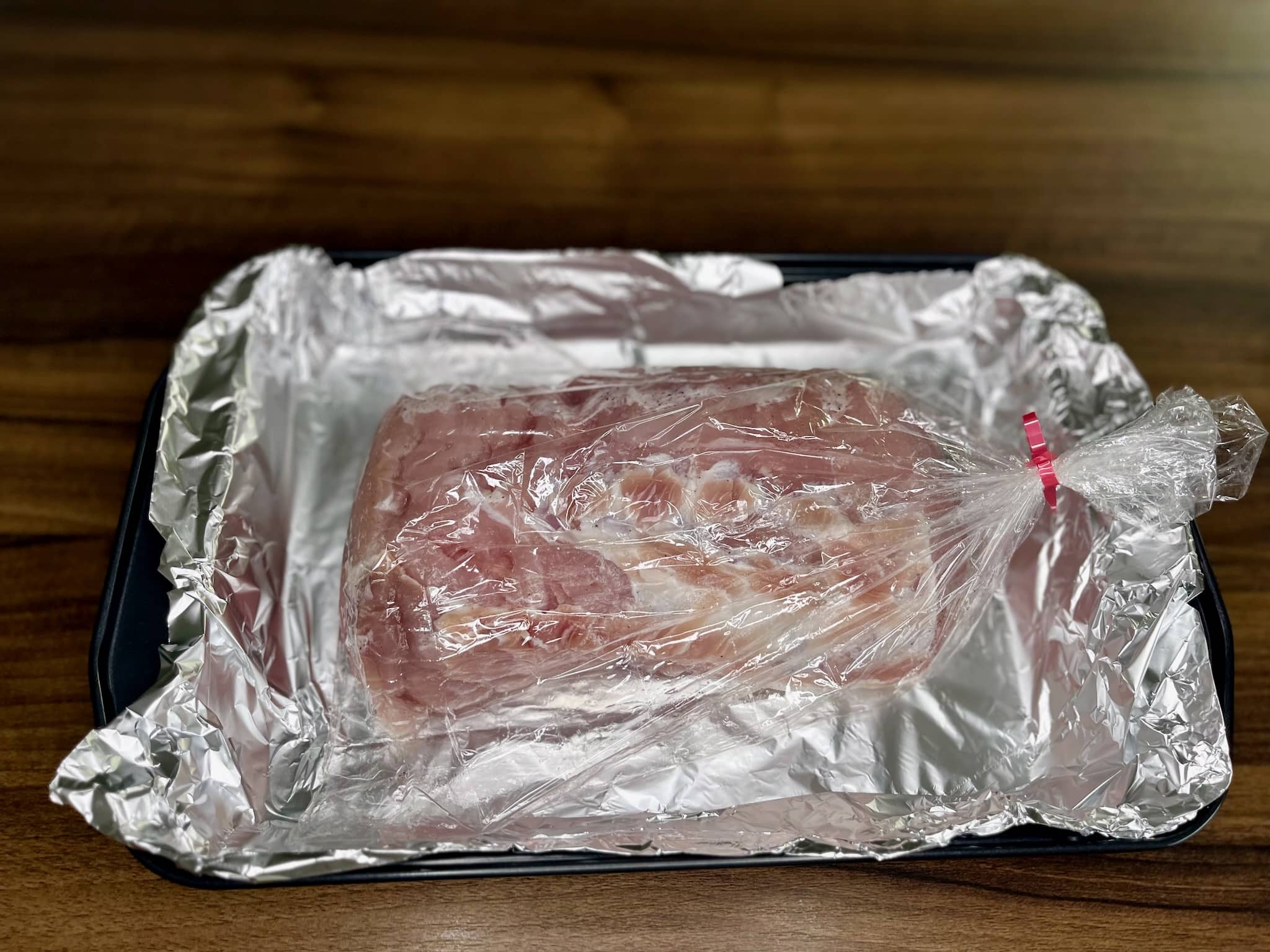 Marinated pork loin in a roasting bag on a lined with aluminium foil baking tray