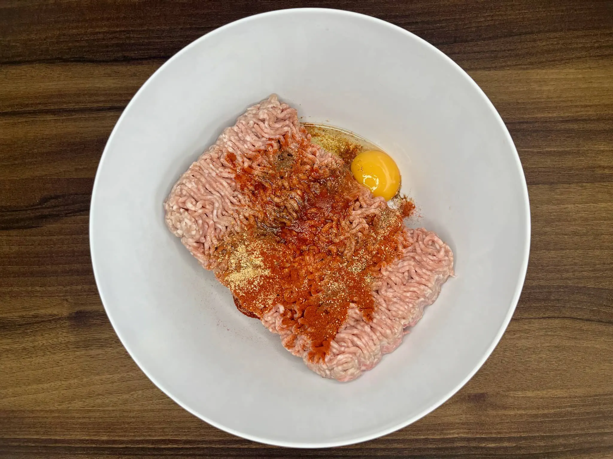 A plastic bowl contains pork mince, egg, and spices, ready to be mixed.