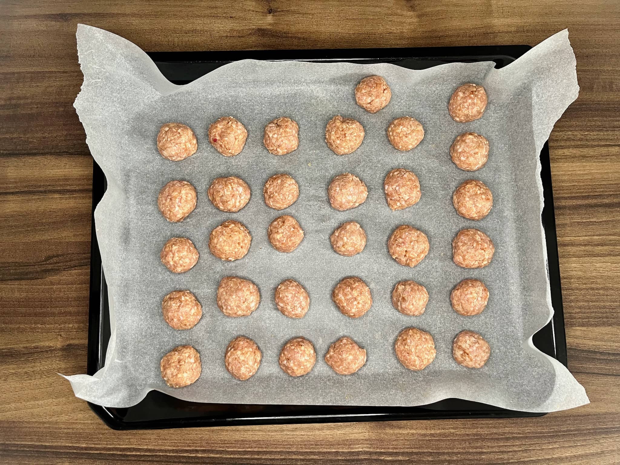 A large baking tray holds formed pork mince balls, ready to be baked in the oven.