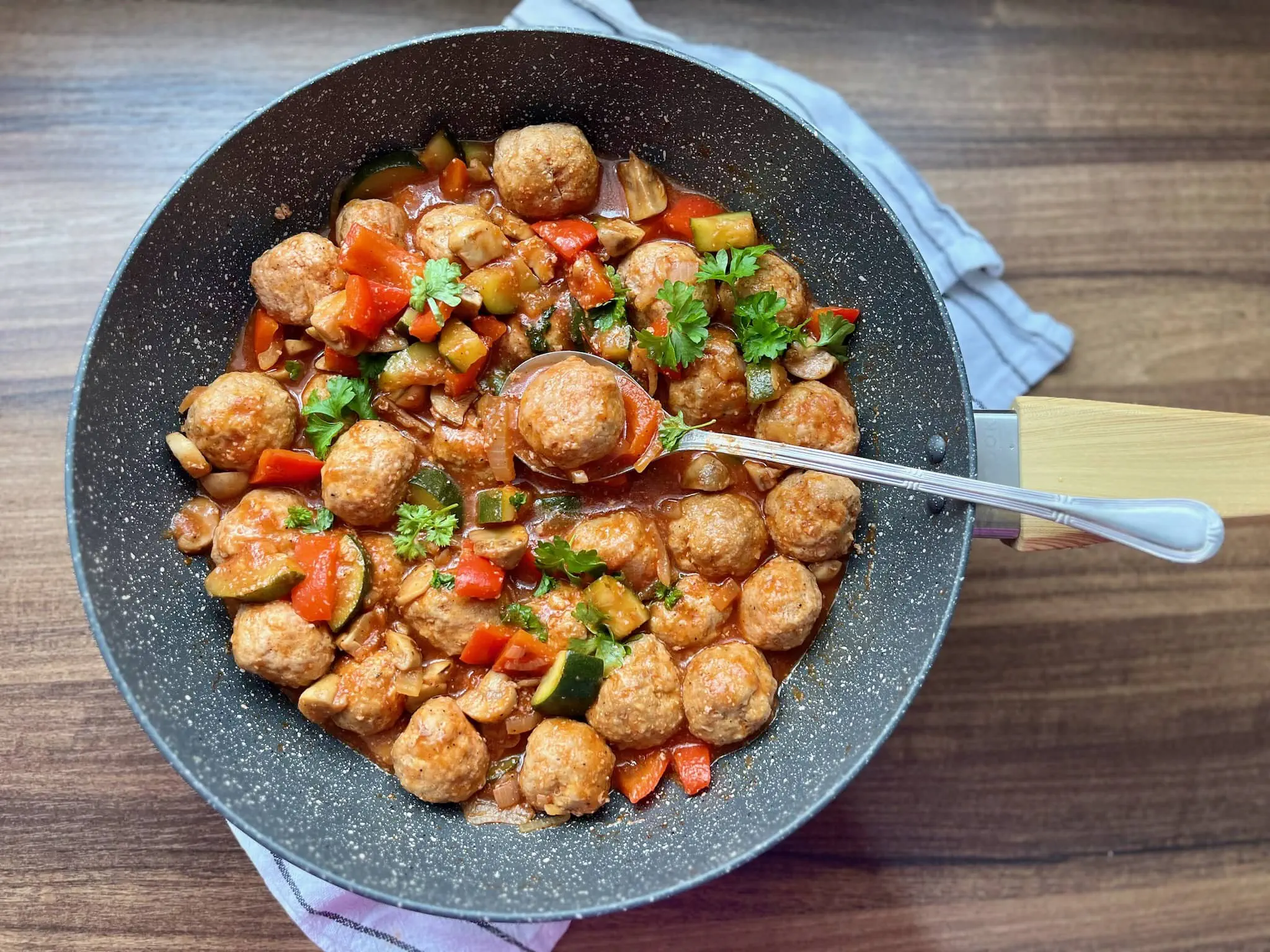 A pan of meatballs in vegetable stew, garnished with fresh parsley, ready to be served.