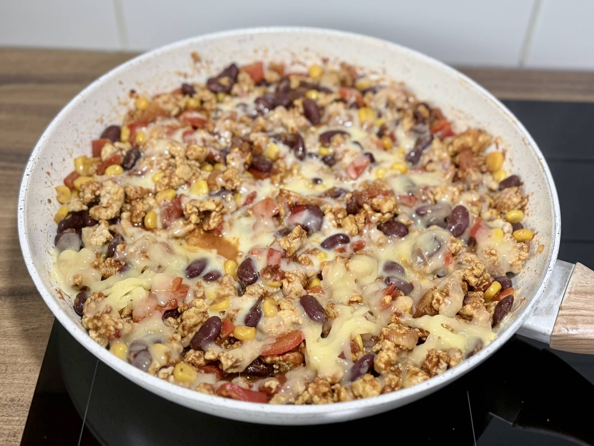 Grated cheese added to the ingredients in a skillet, nicely melted on the top