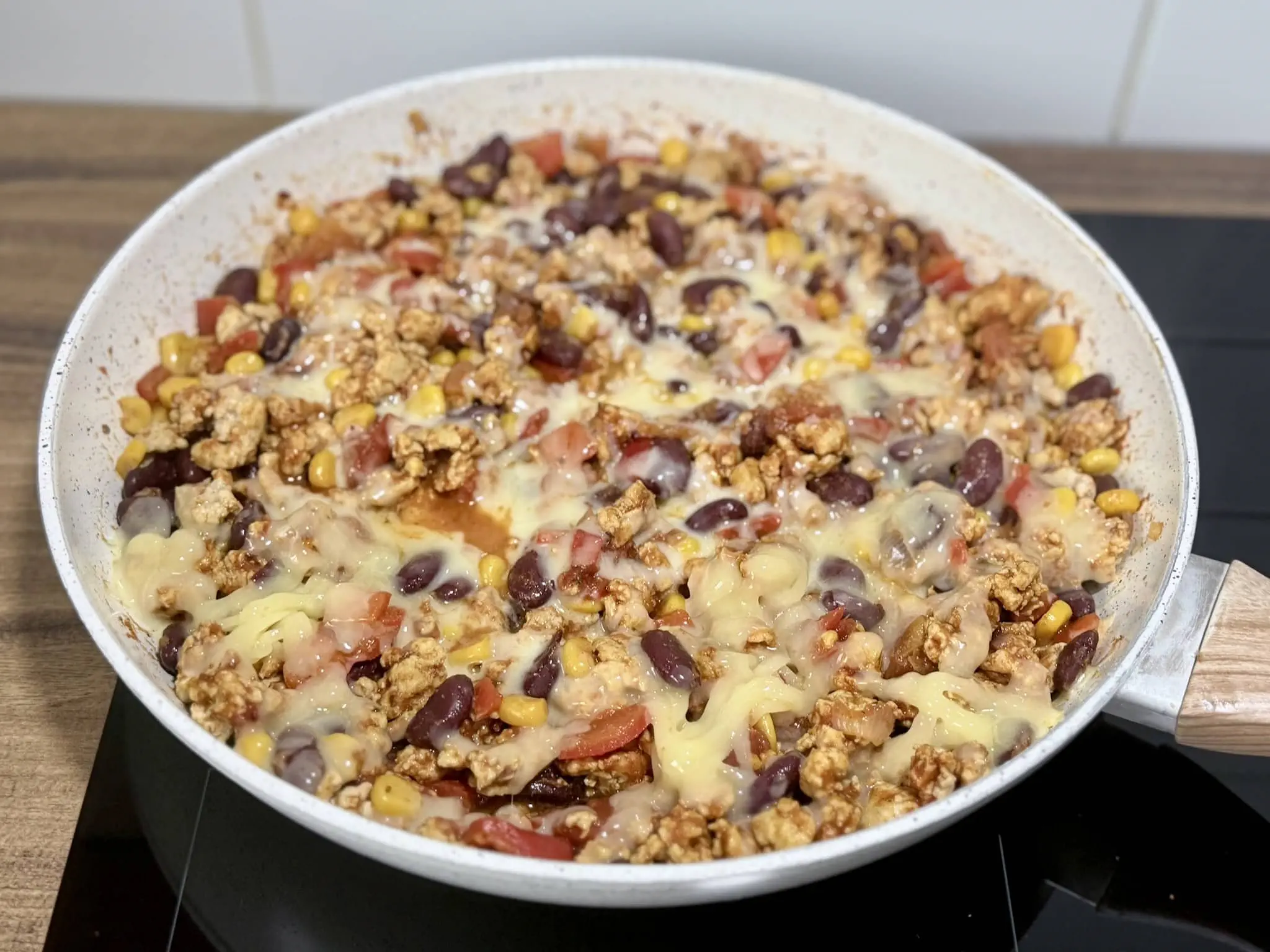 Grated cheese added to the ingredients in a skillet, nicely melted on the top