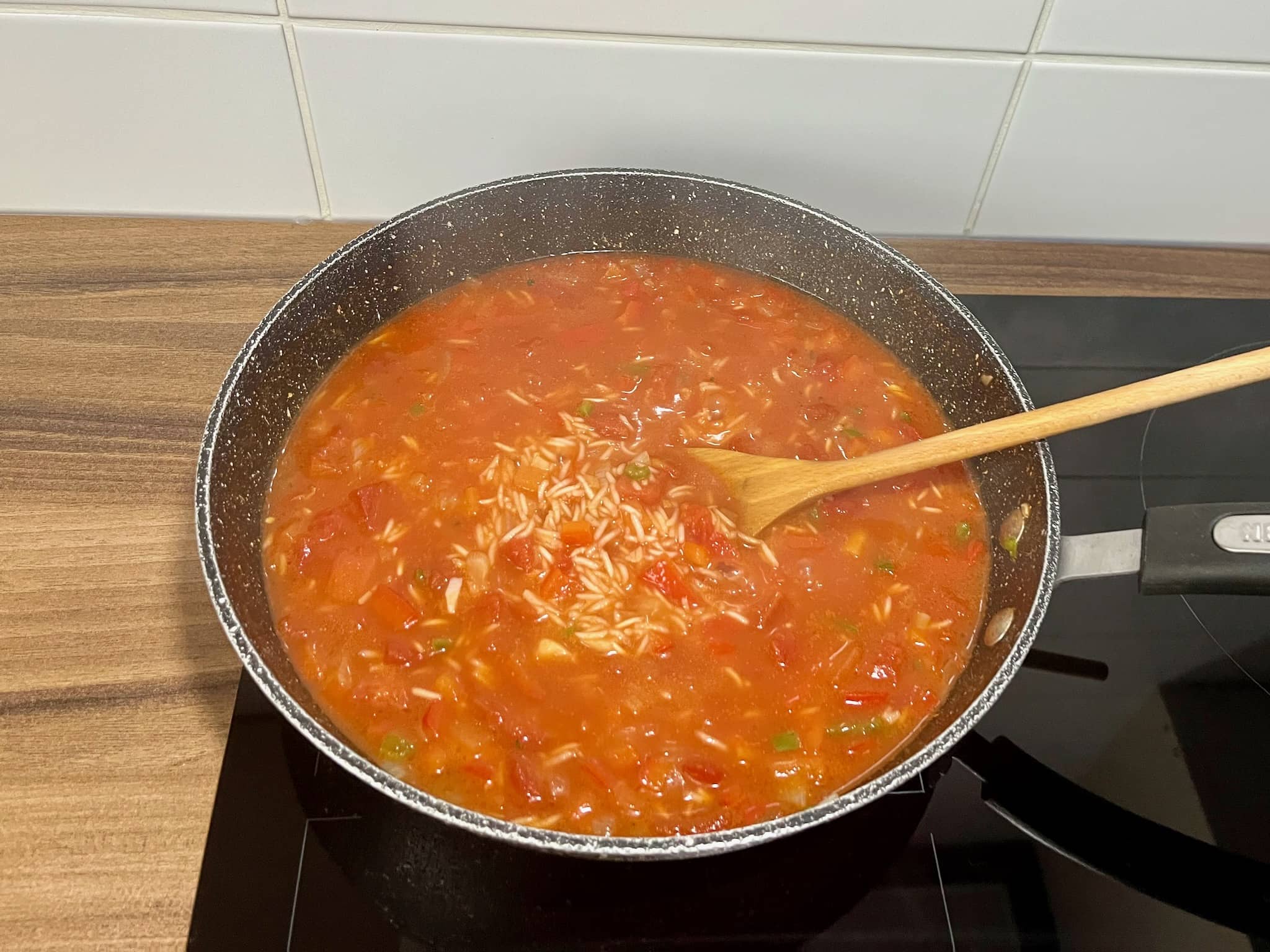 Peppers, onion, garlic, rice and chopped tomatoes with chicken broth in a pan
