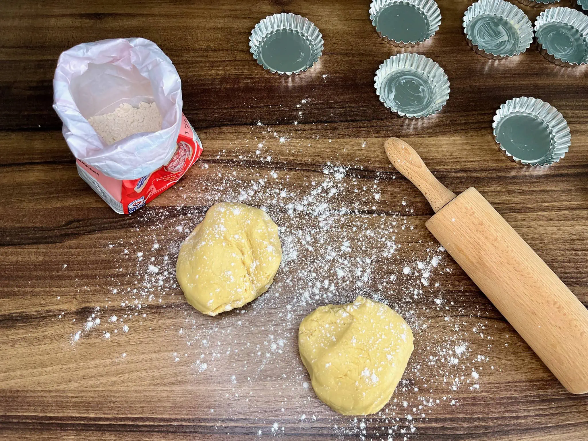 Two pieces of dough are on the floured tabletop, ready to be made into tarts