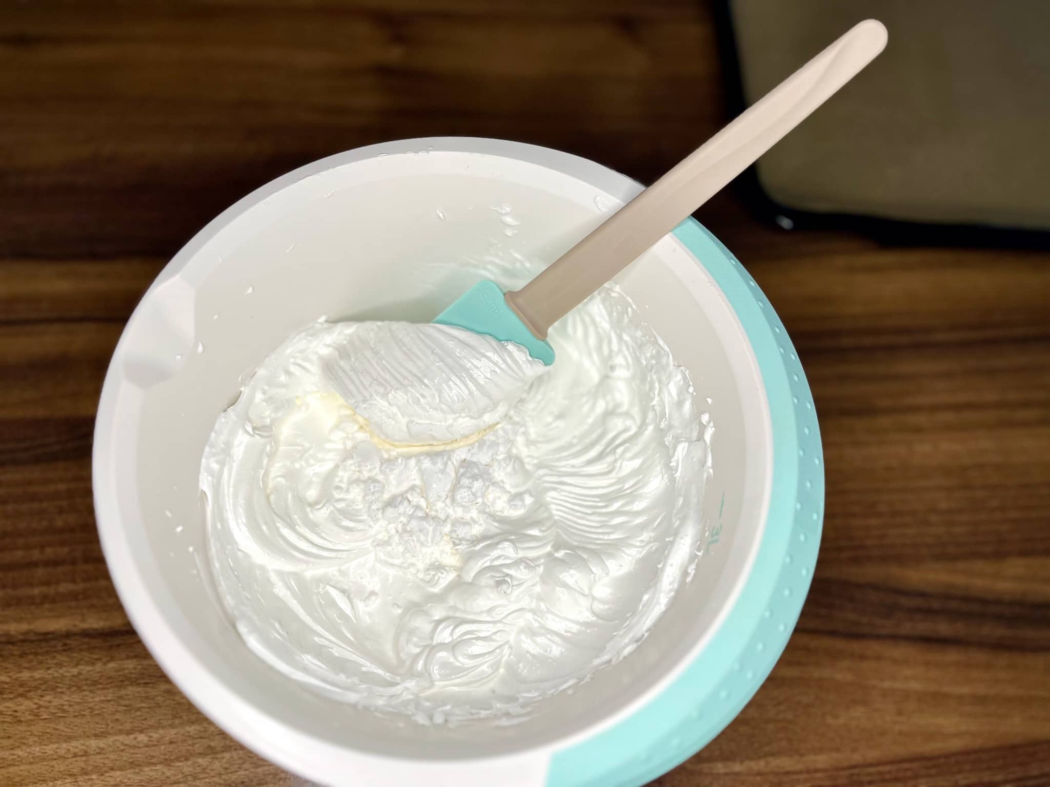Stiff egg whites are folded into a bowl with potato flour using a spatula