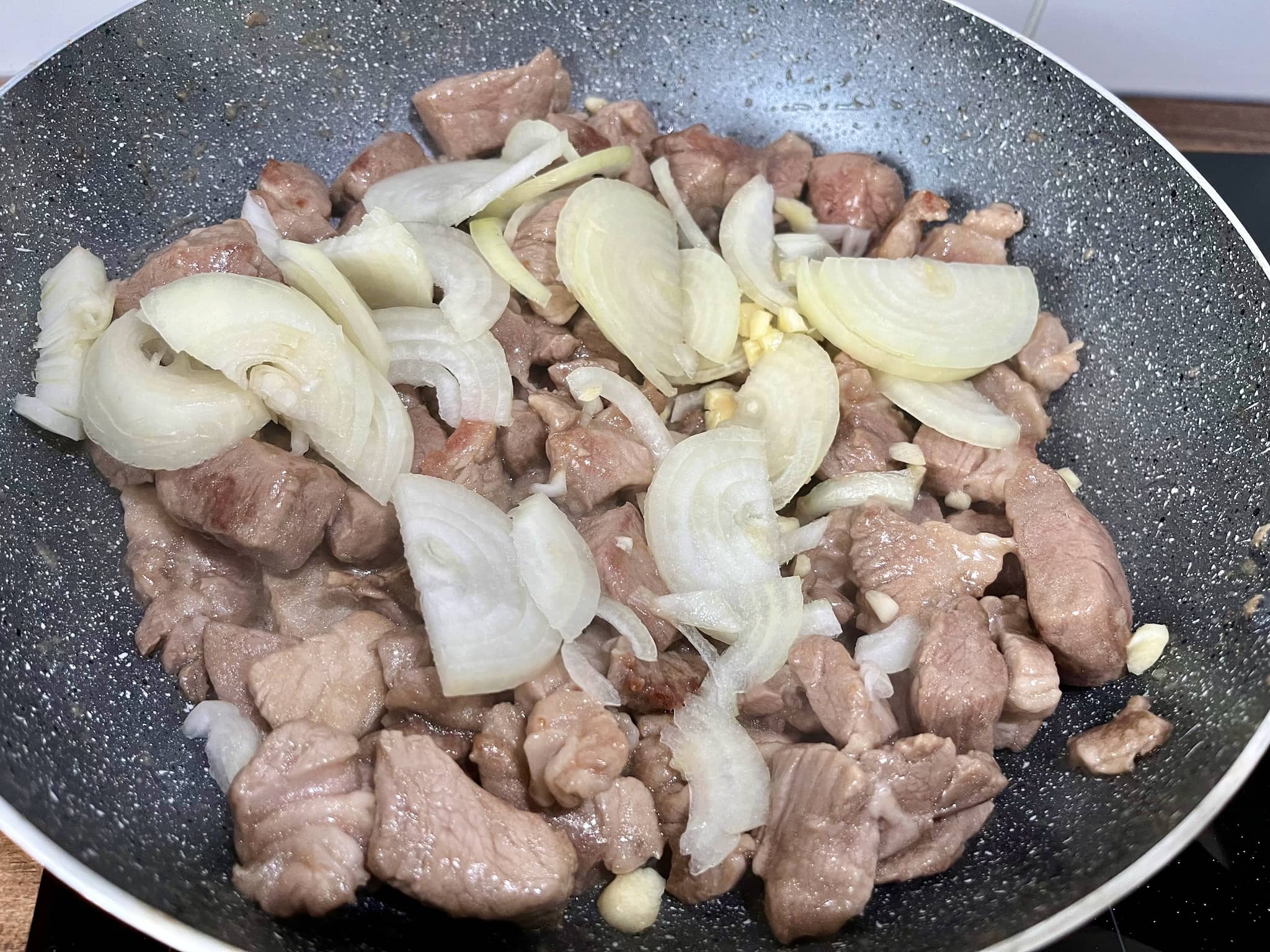 Fried pork in a pan with added chopped onion and crushed garlic