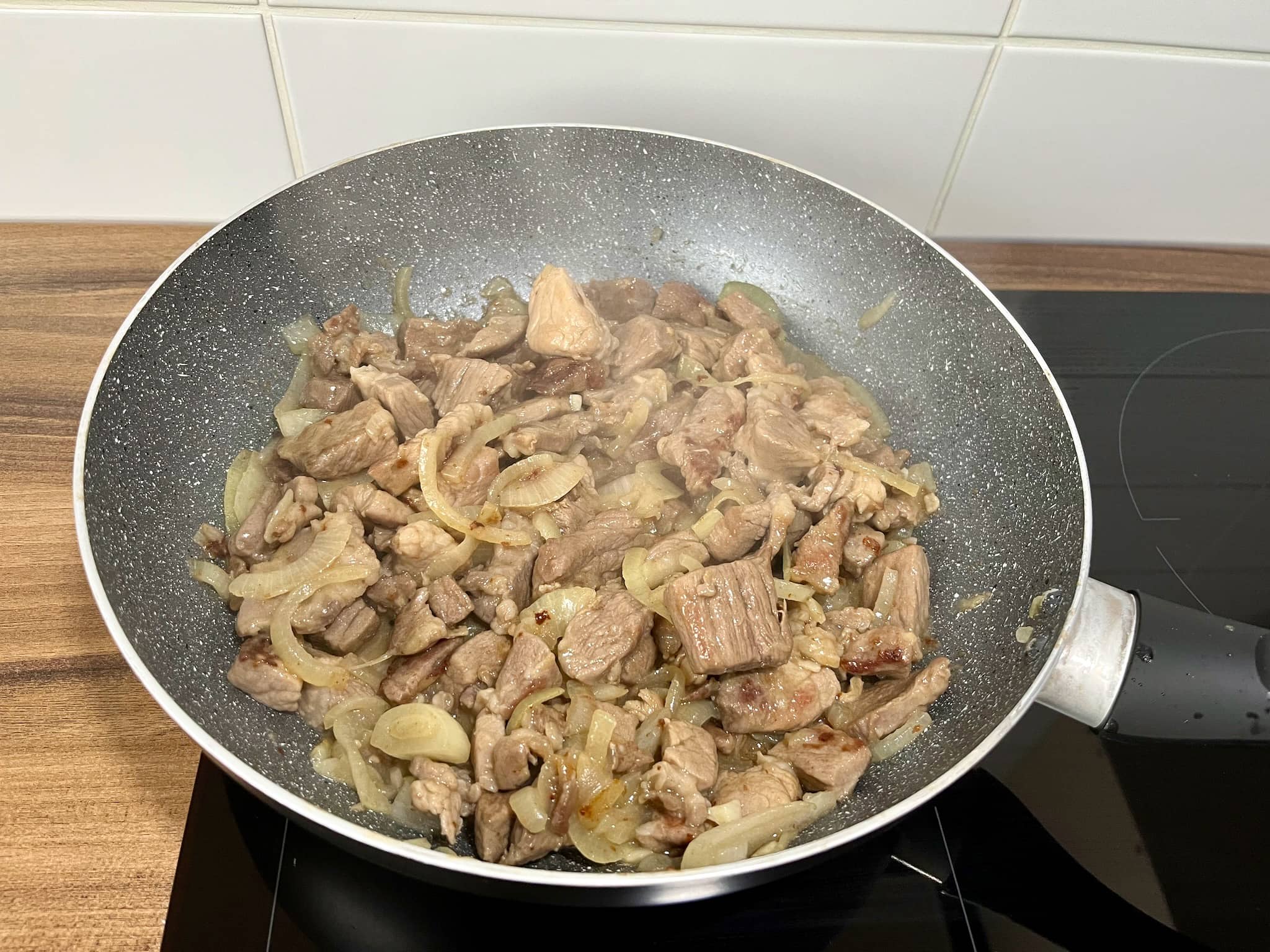Fried pork with softened onion in a pan