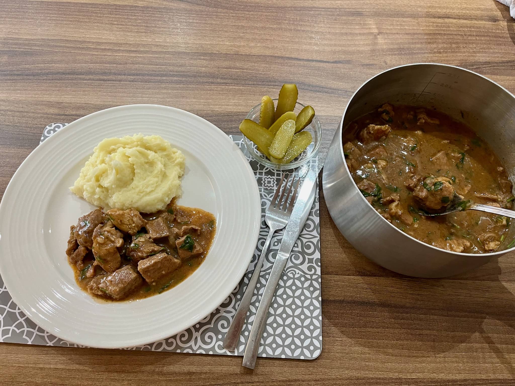 Pork goulash served with mashed potatoes and gherkins on the side