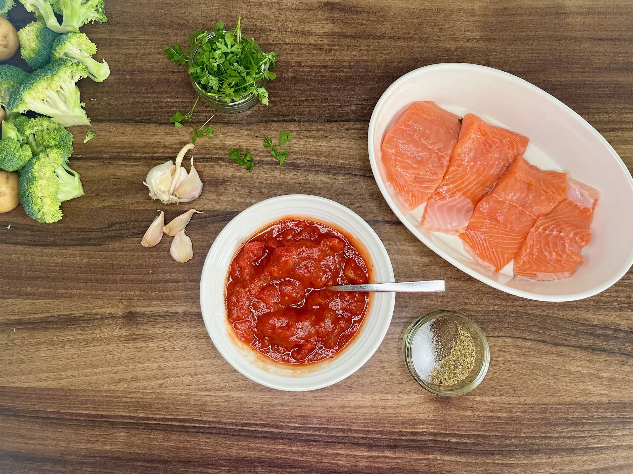 Tomatoes are in a bowl, spices are on the side, and salmon is lined in an ovenproof baking dish, ready to make oven-baked salmon in tomato sauce