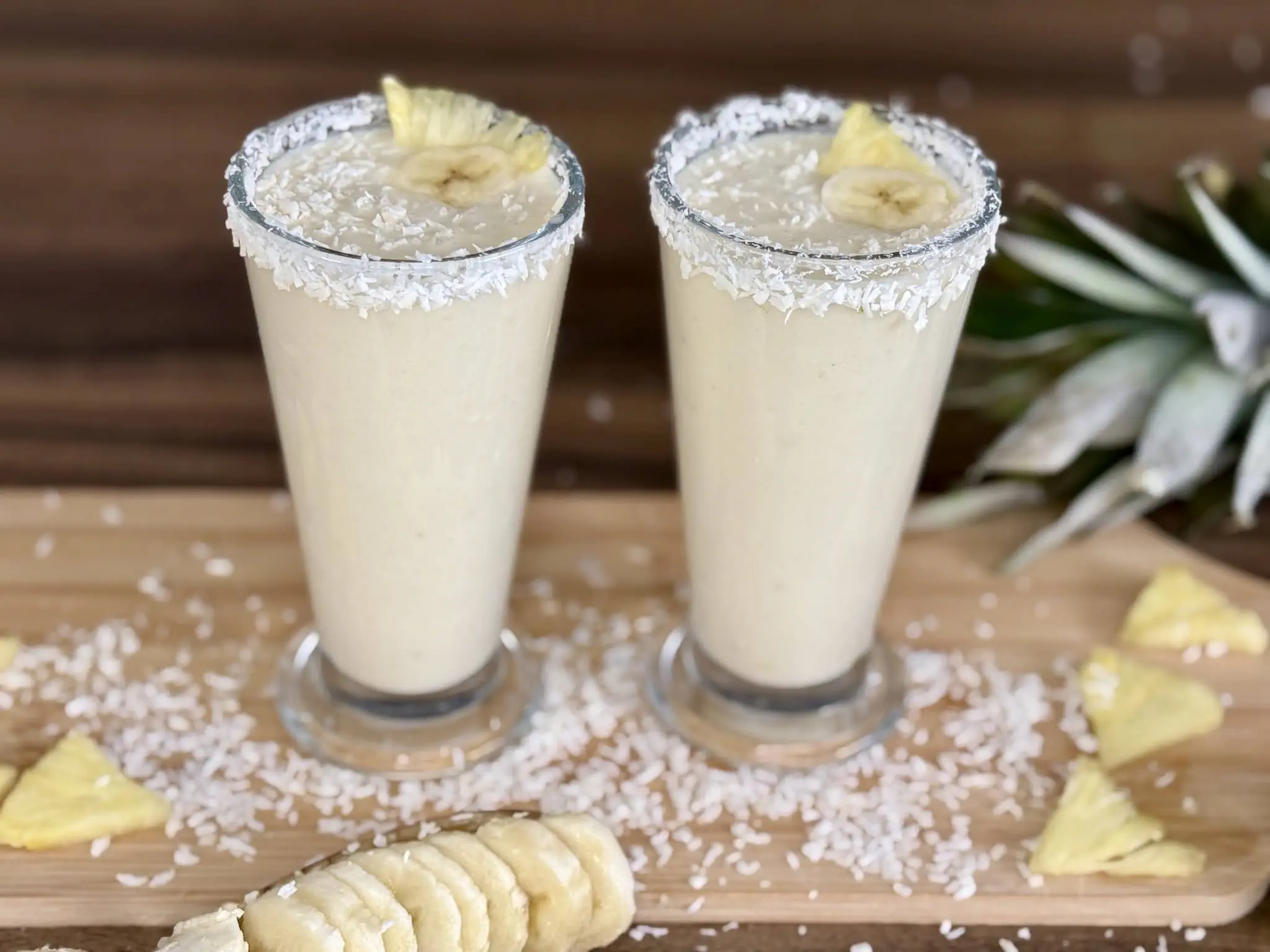 Smoothie inspirowane Pina Colada w wysokich szklankach ozdobione plasterkami banana i wiórkami kokosowymi