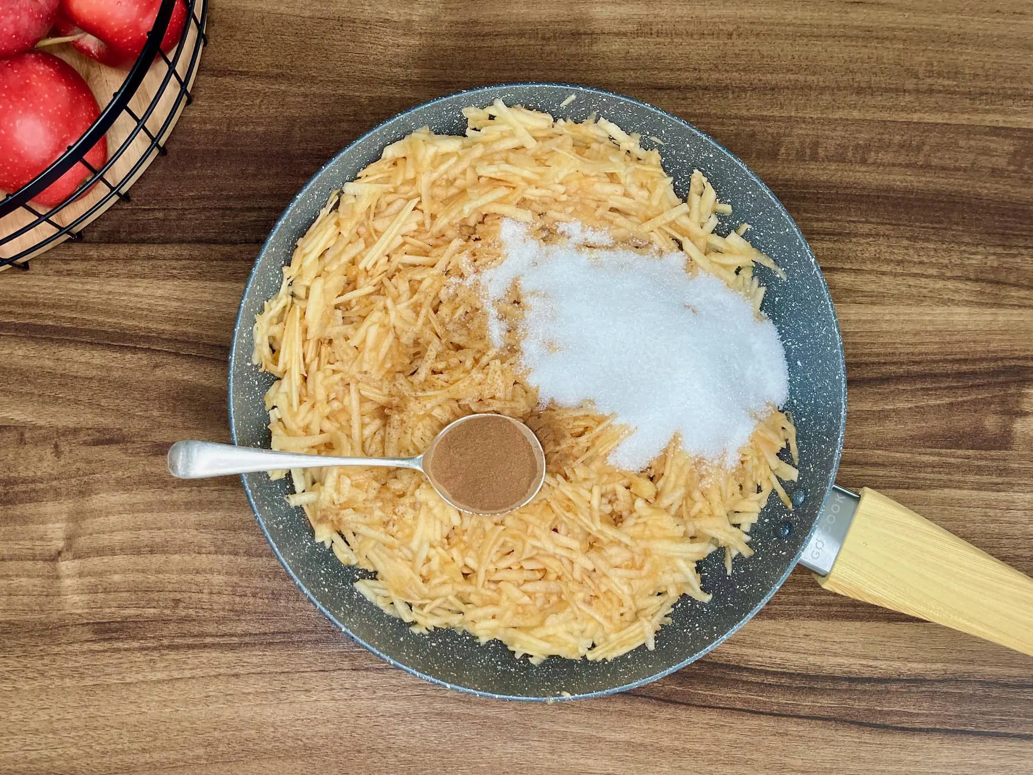 Grated apples are placed in a pan and sprinkled with sugar