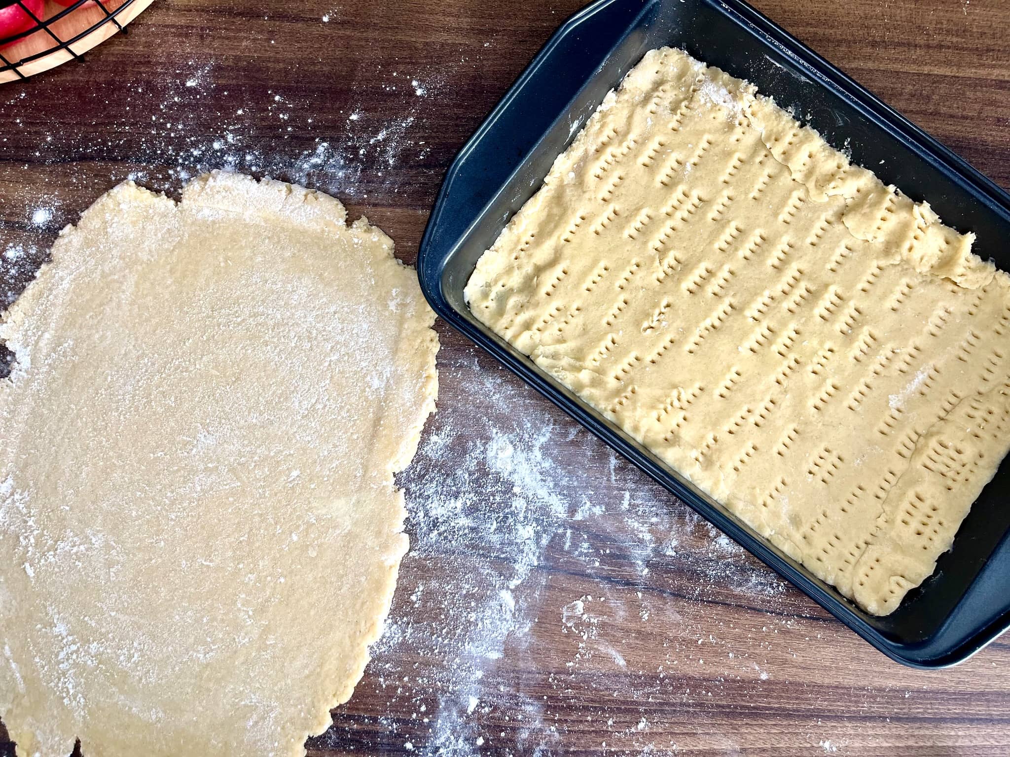 Portion of the dough is pressed into a greased baking tin, while the other remains on a floured surface