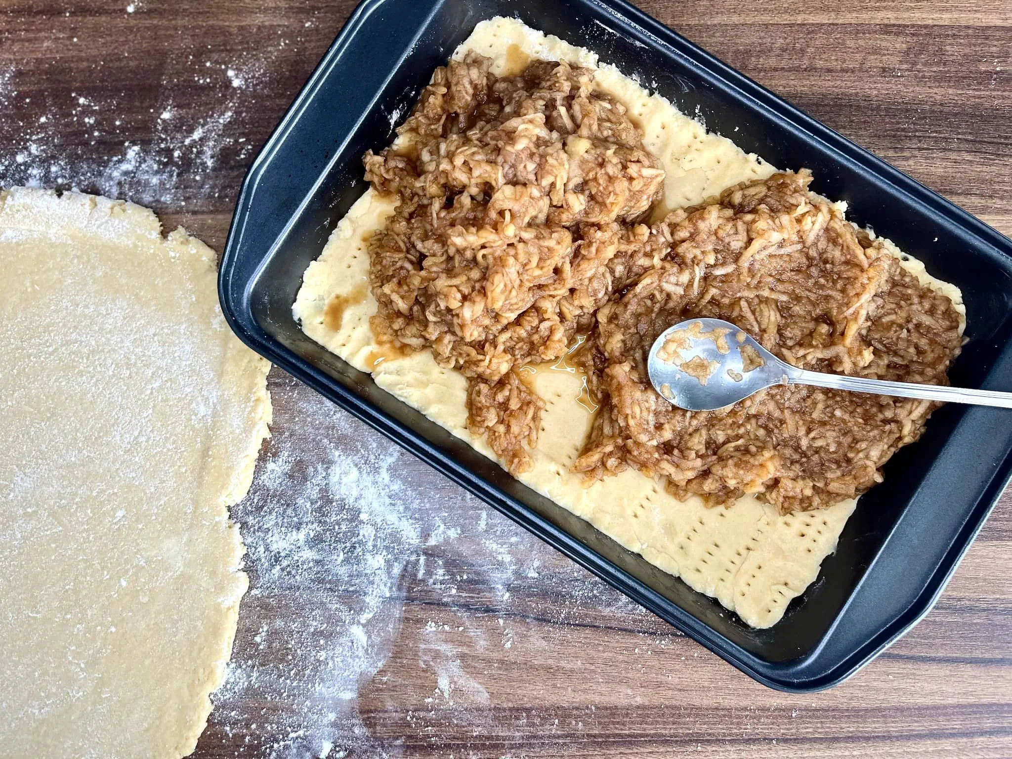 The cooked grated apples are evenly distributed over the dough in the baking tin