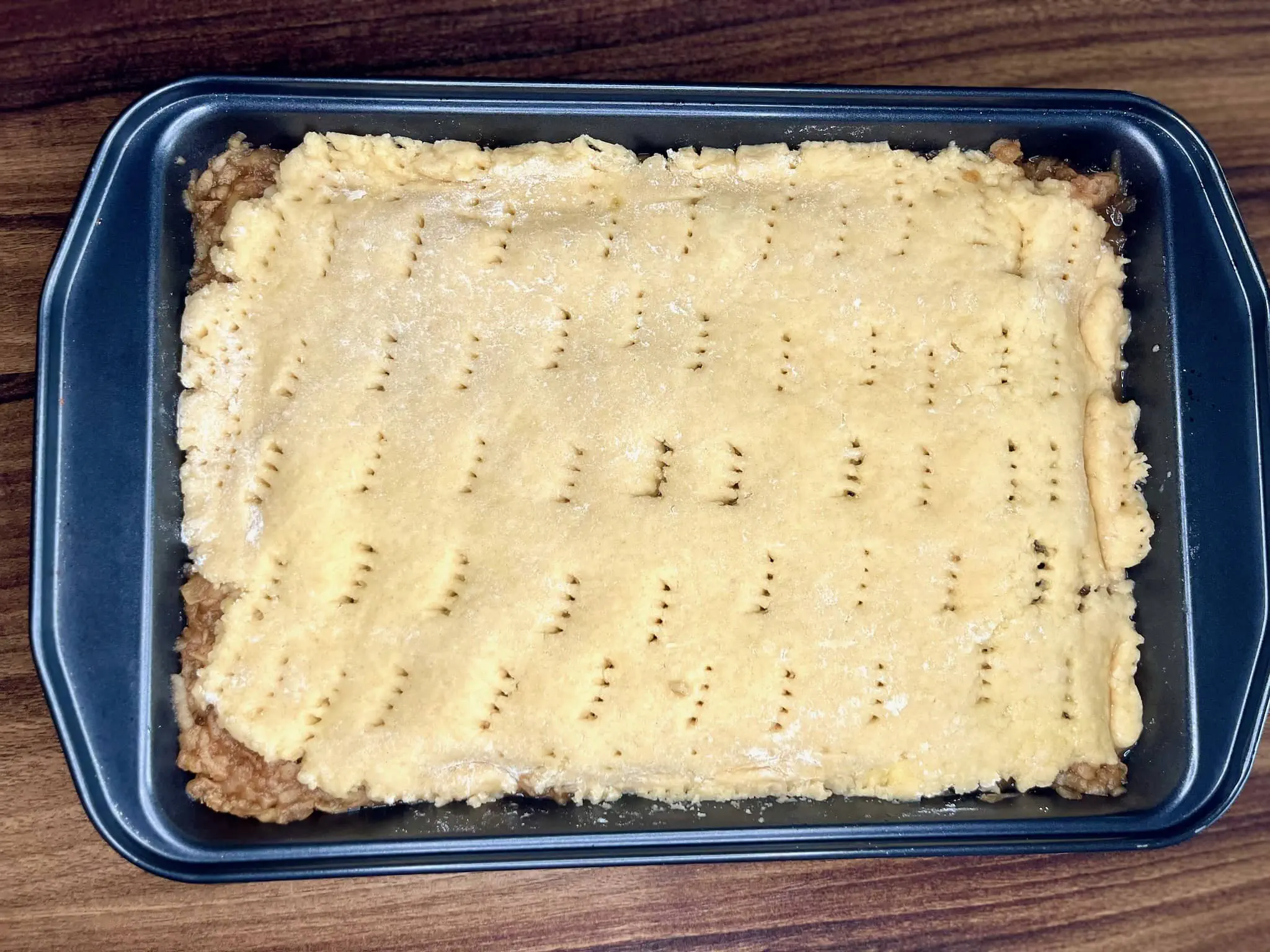 The remaining portion of the dough is gently placed over the apples in the baking tin