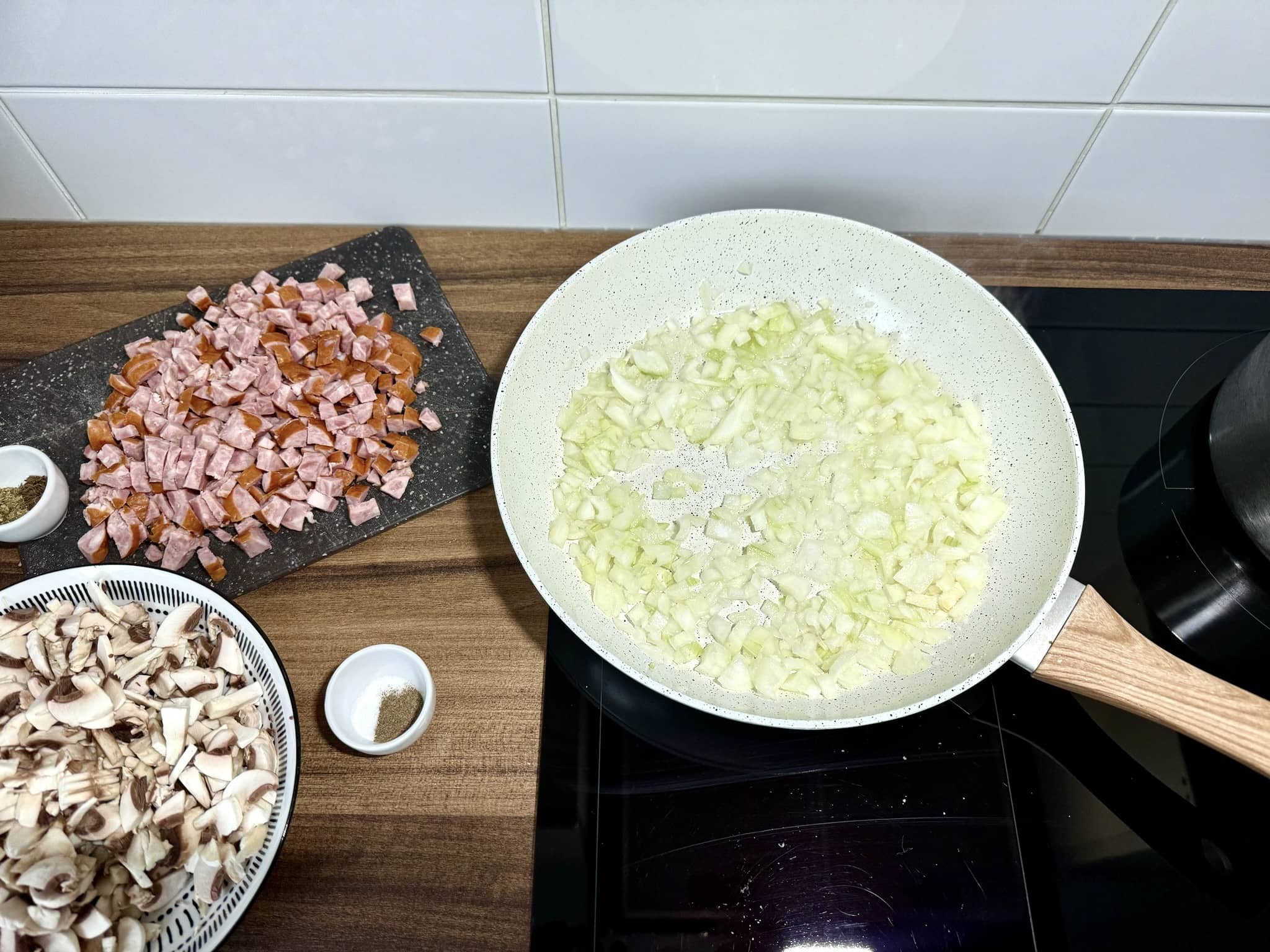 Pokrojona kiełbasa na desce do krojenia i cebula smażąca się na patelni