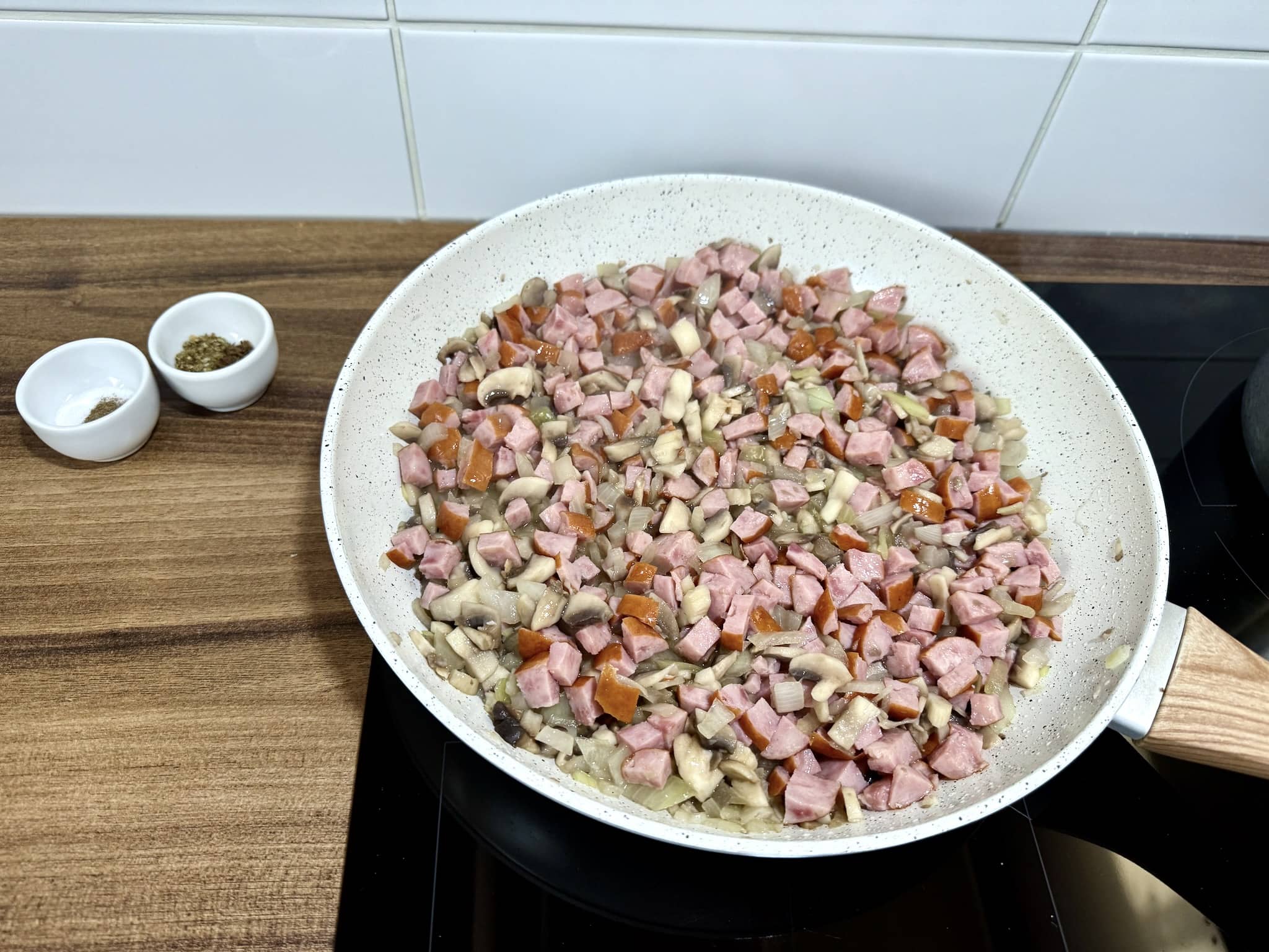 Kawałki kiełbasy śląskiej dodane do patelni z cebulą i pieczarkami