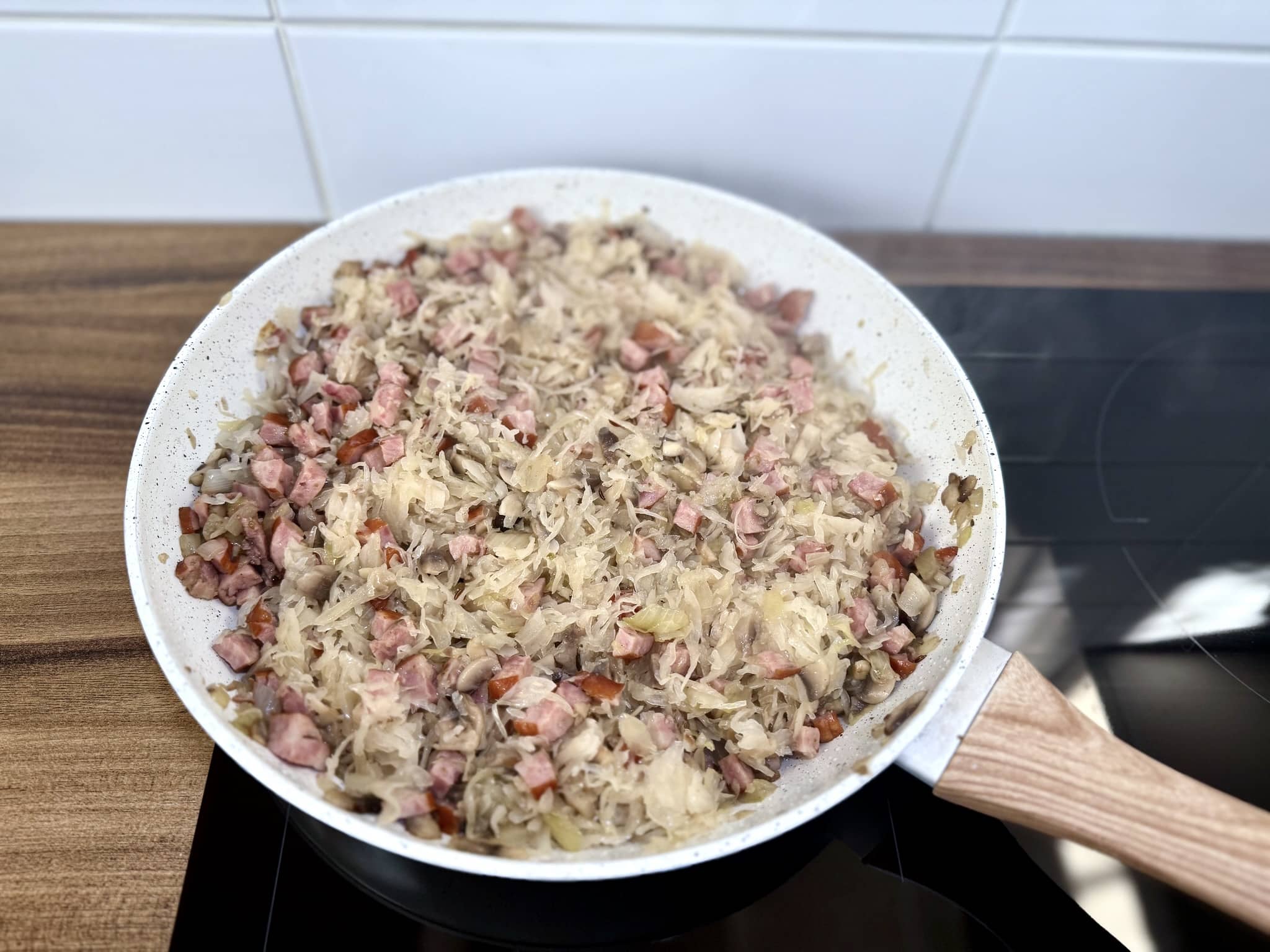Kapusta kiszona dodana do kiełbasy, cebuli i pieczarek na patelni