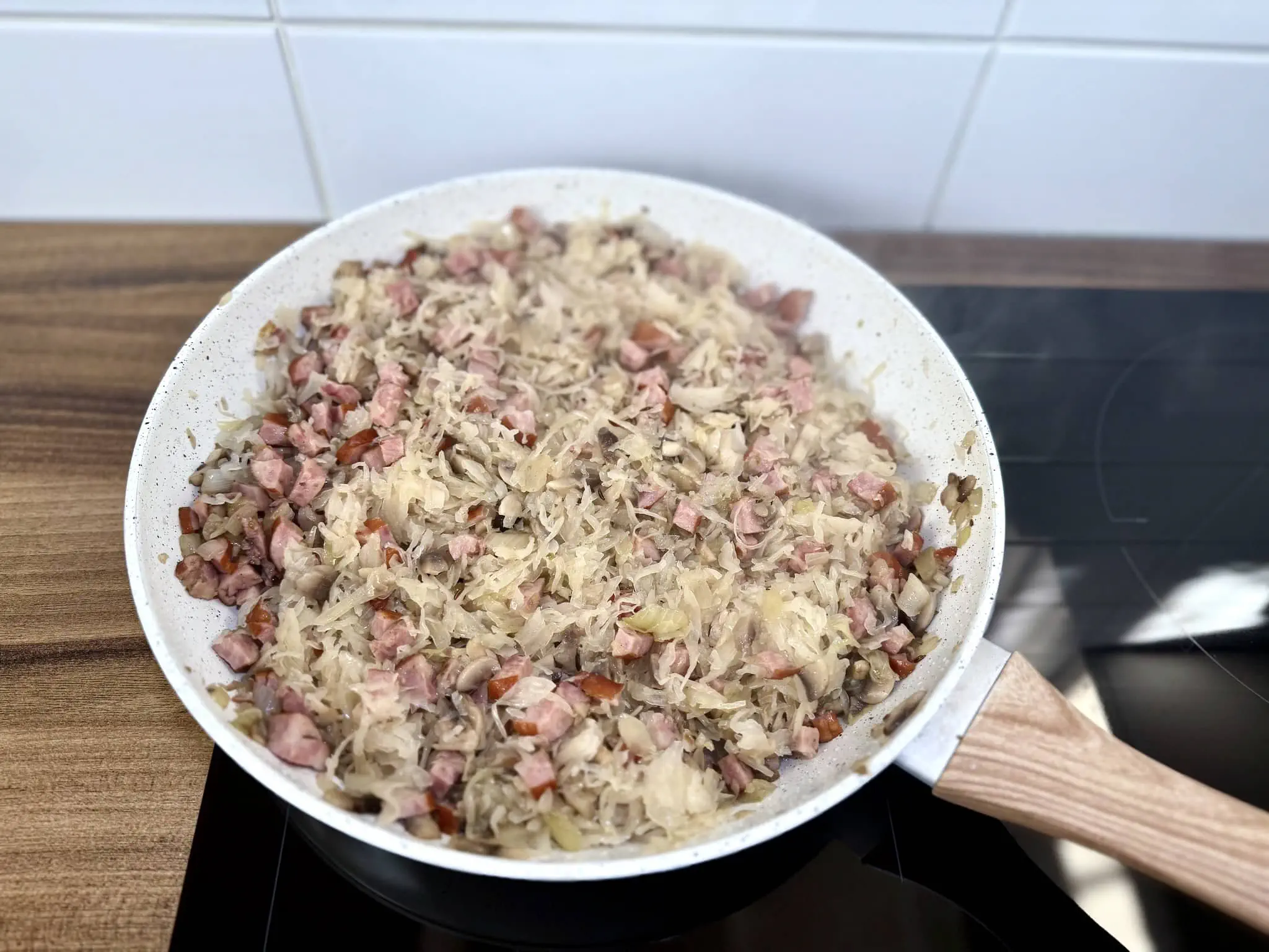 Kapusta kiszona dodana do kiełbasy, cebuli i pieczarek na patelni