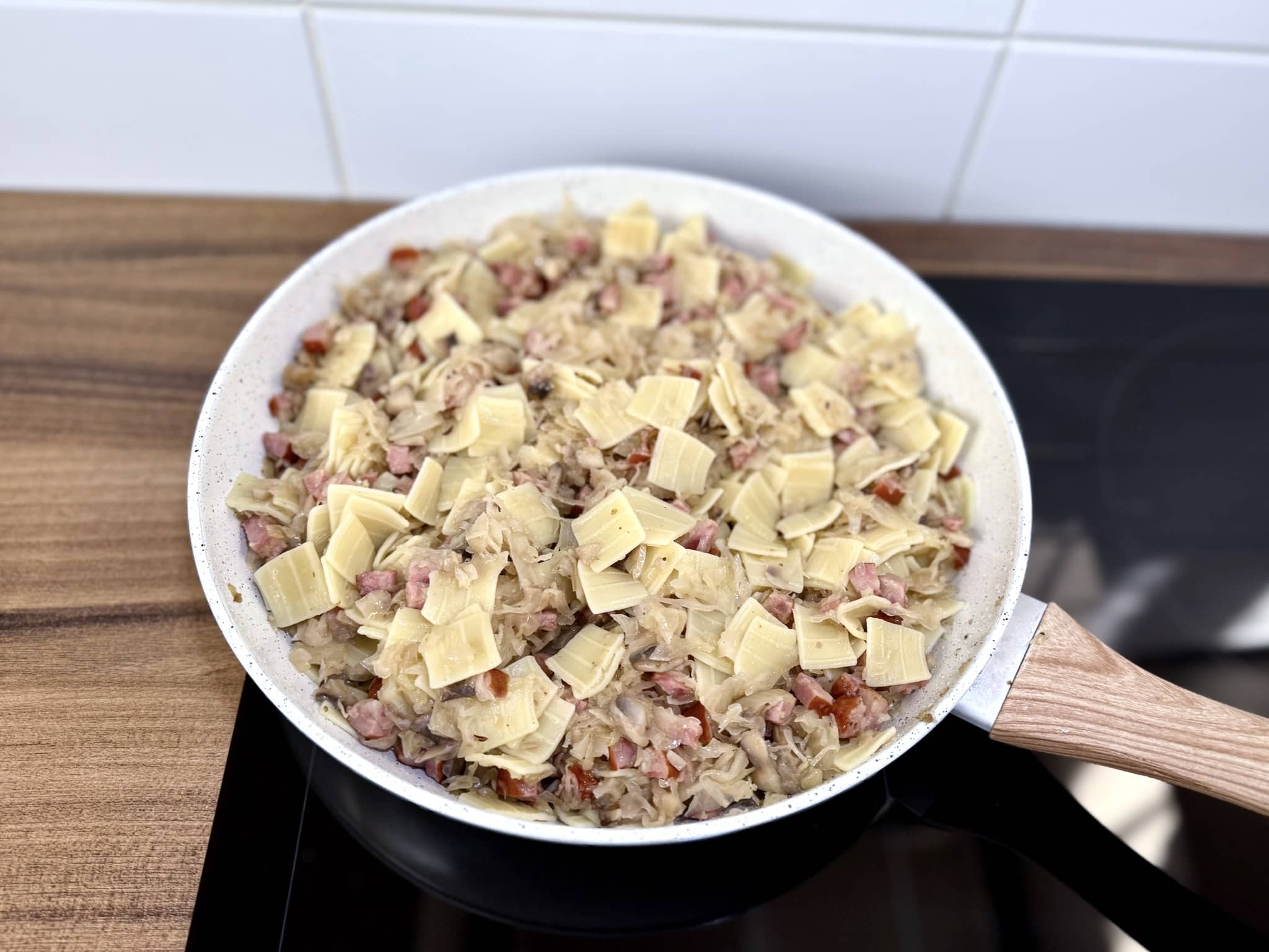 Makaron quadretti dodany do patelni z kapustą kiszoną, kiełbasą, cebulą i pieczarkami