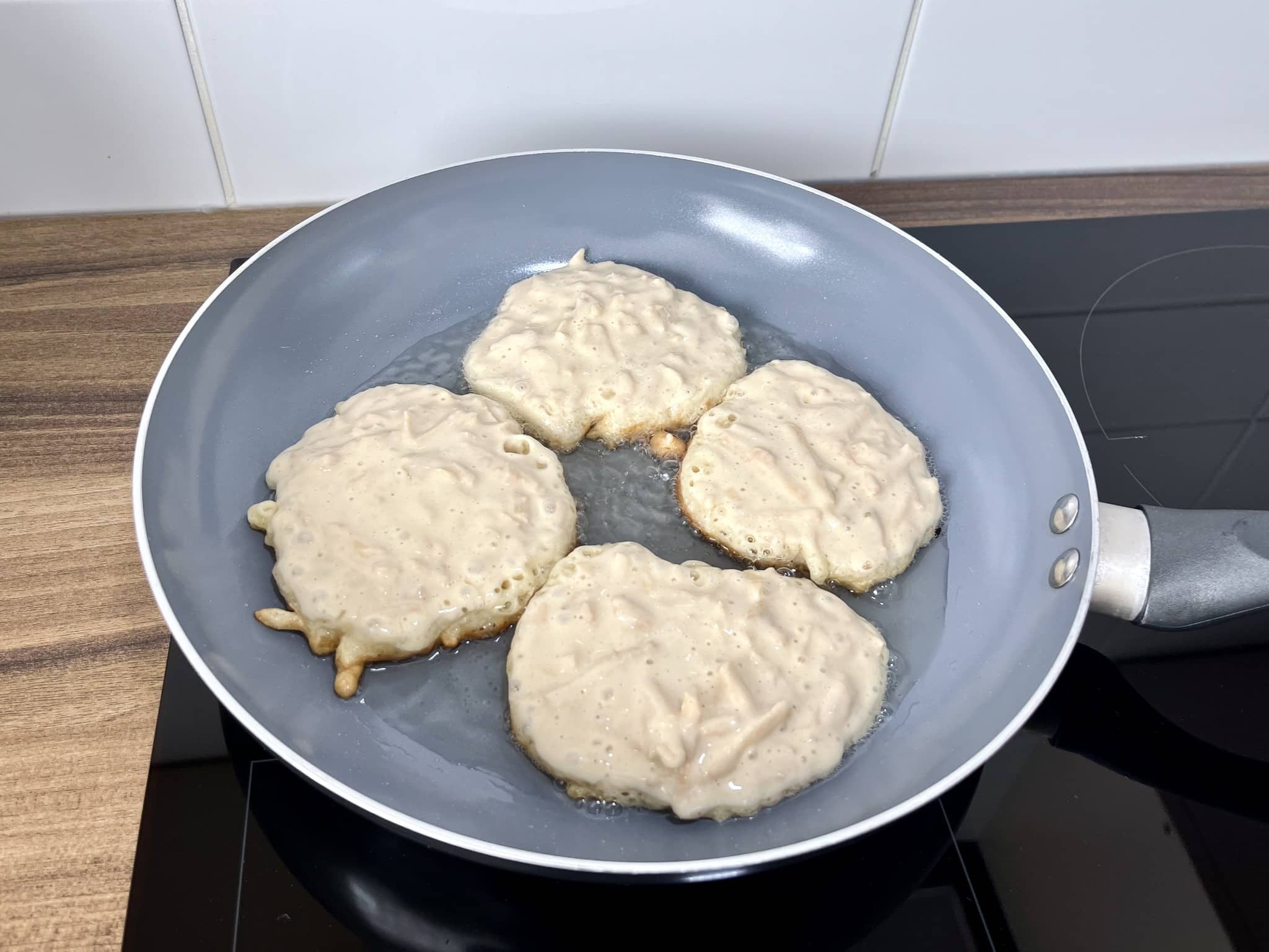 Cztery porcje placuszków z jabłkami smażące się na patelni