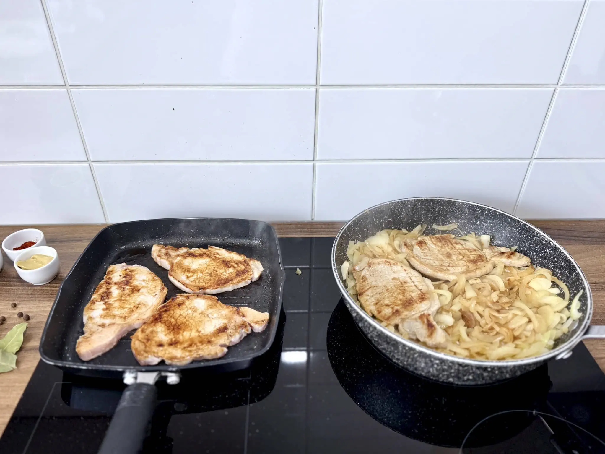 Kotlety ze schabu smażące się na patelni z niektórymi kawałkami już na cebuli na innej patelni