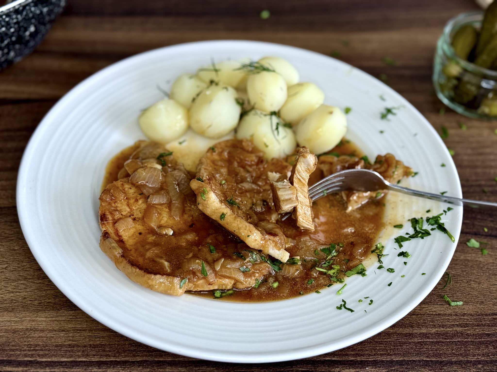 Pork Chops in Onion Sauce garnished with parsley served with potatoes, on a plate