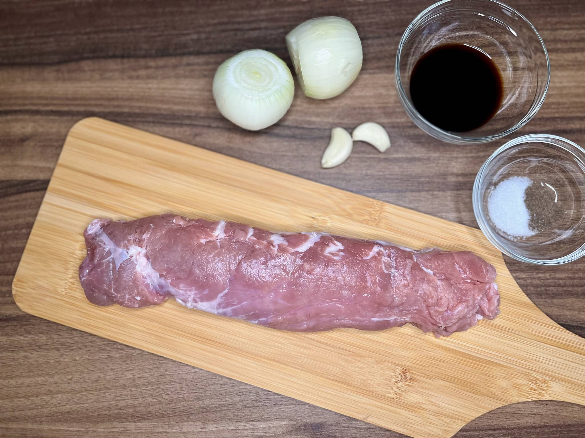 Pork tenderloin on a chopping board with other ingredients on the side