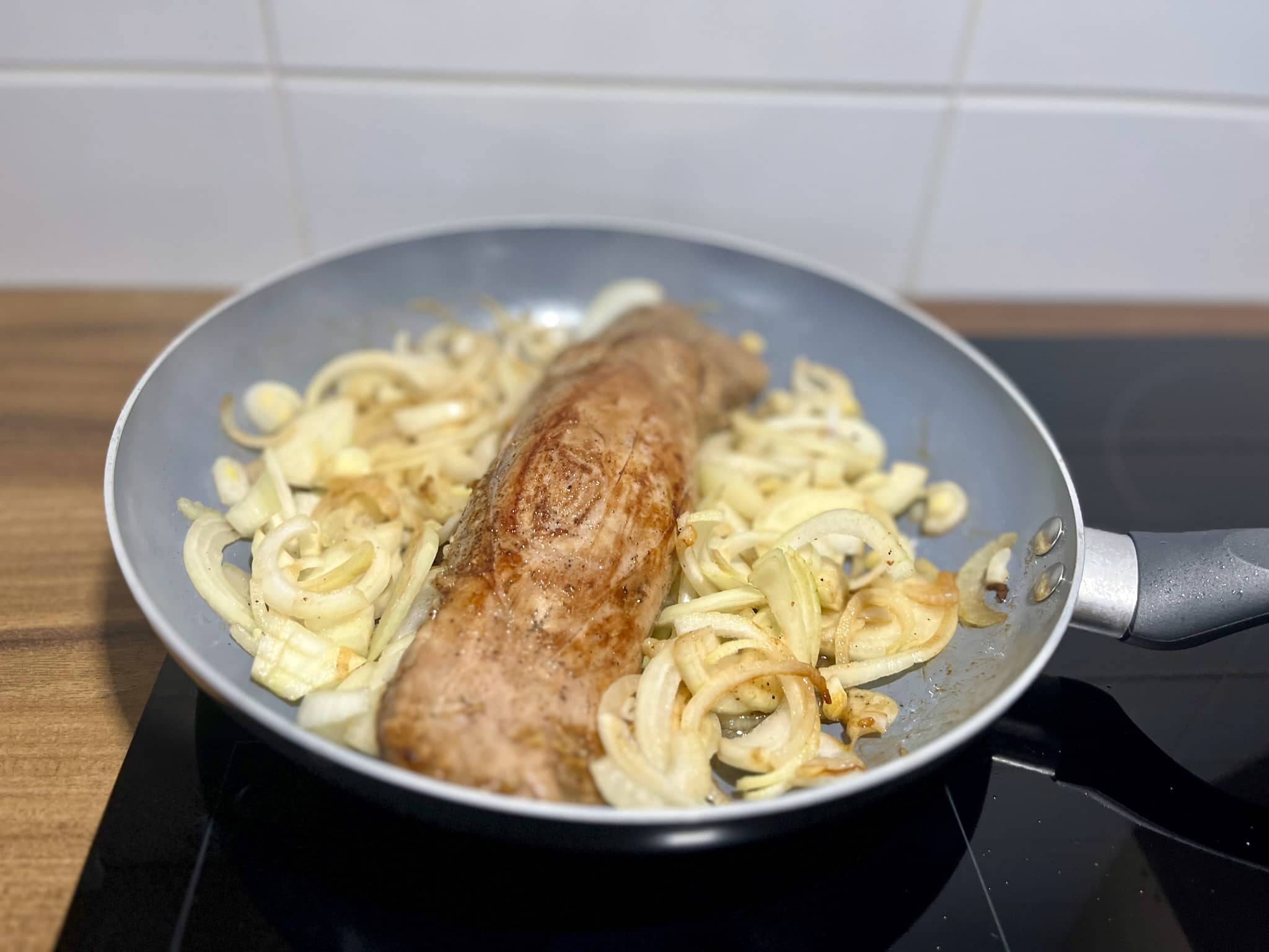 Pork tenderloin frying with onion in a pan
