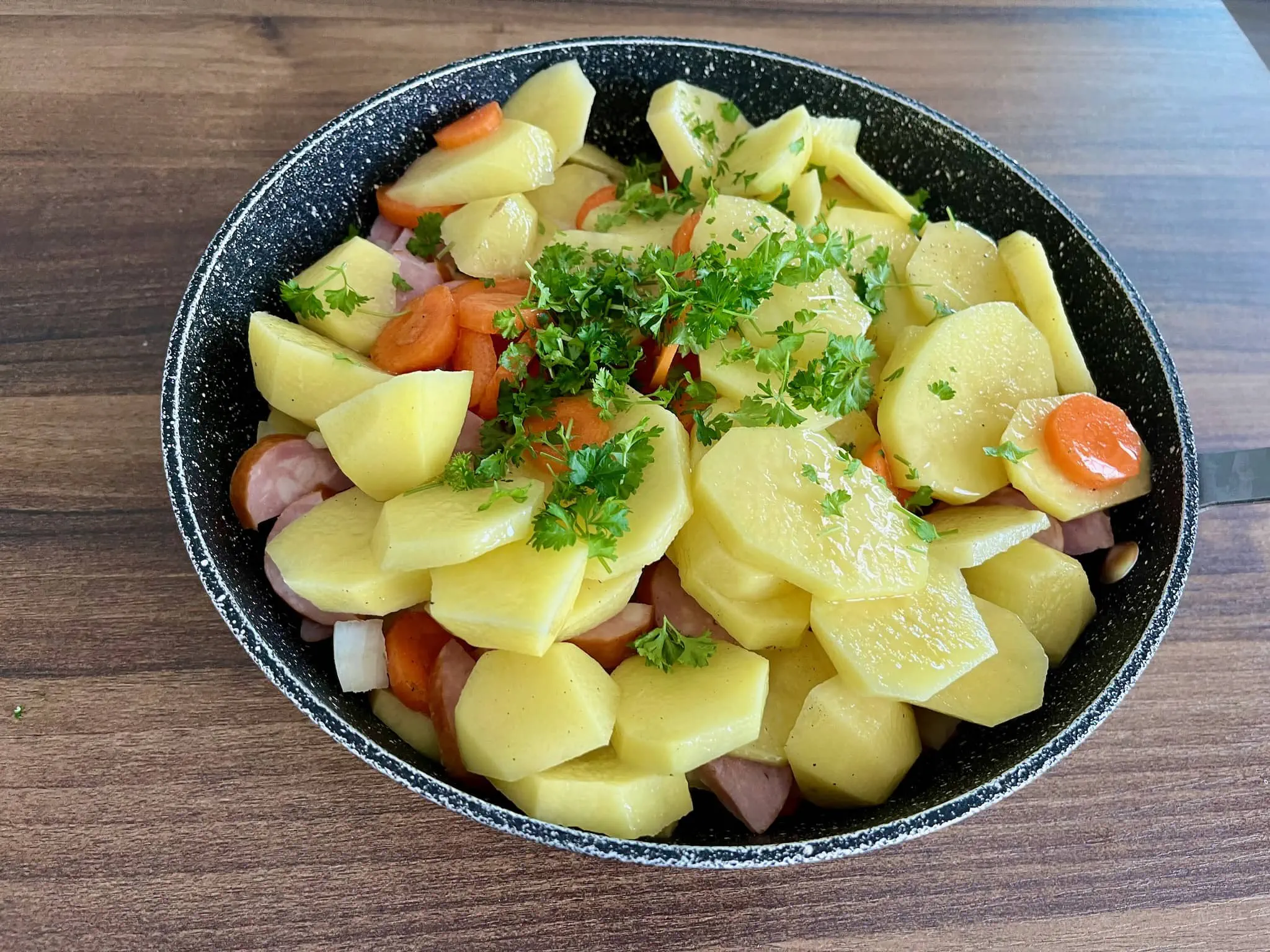 Garnek gotowy do gotowania, ziemniaki, kiełbasa, cebula i marchewka z pietruszką na wierzchu