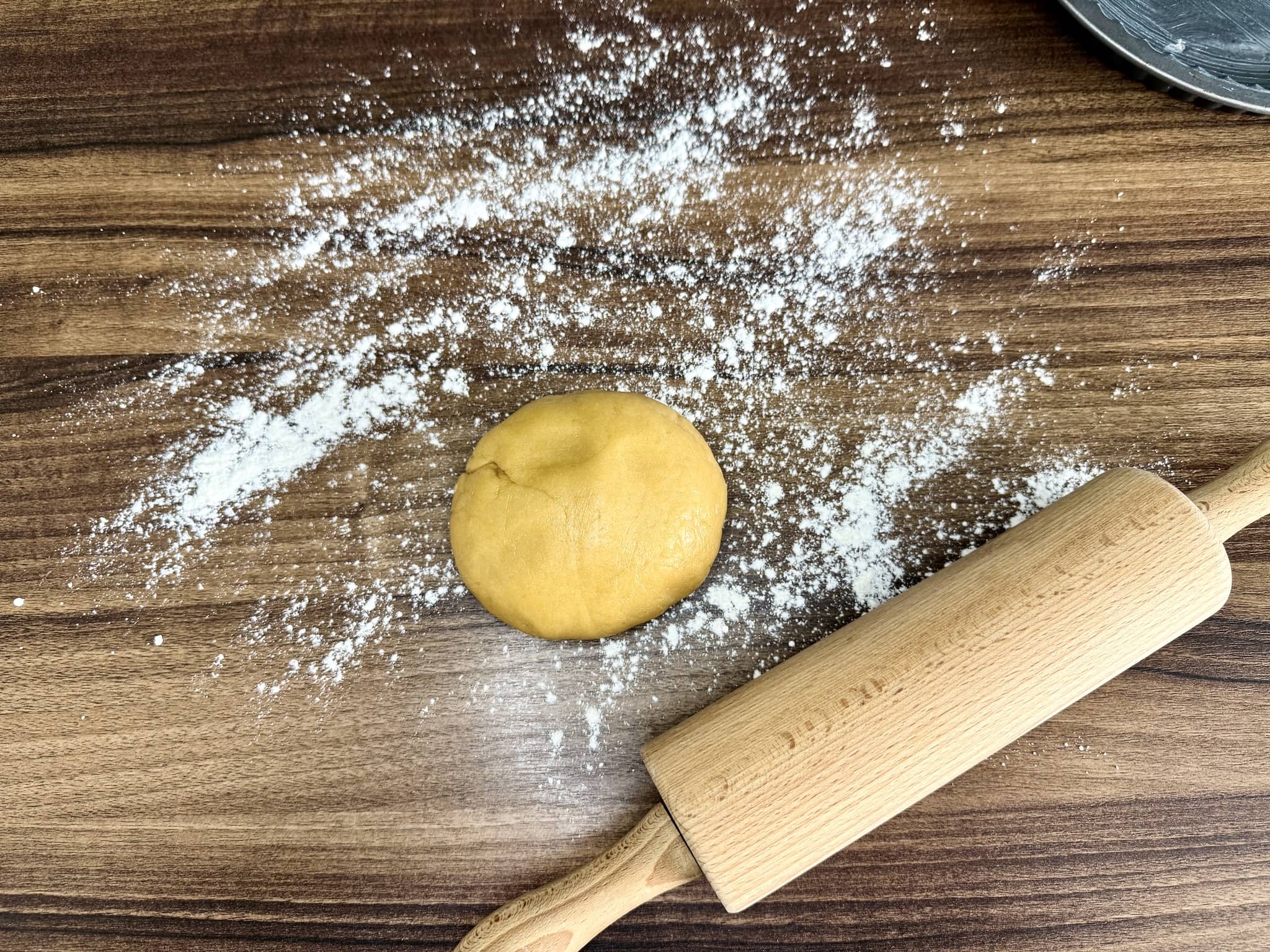 Rested dough on lightly dusted flour tabletop with rolling pin on the side