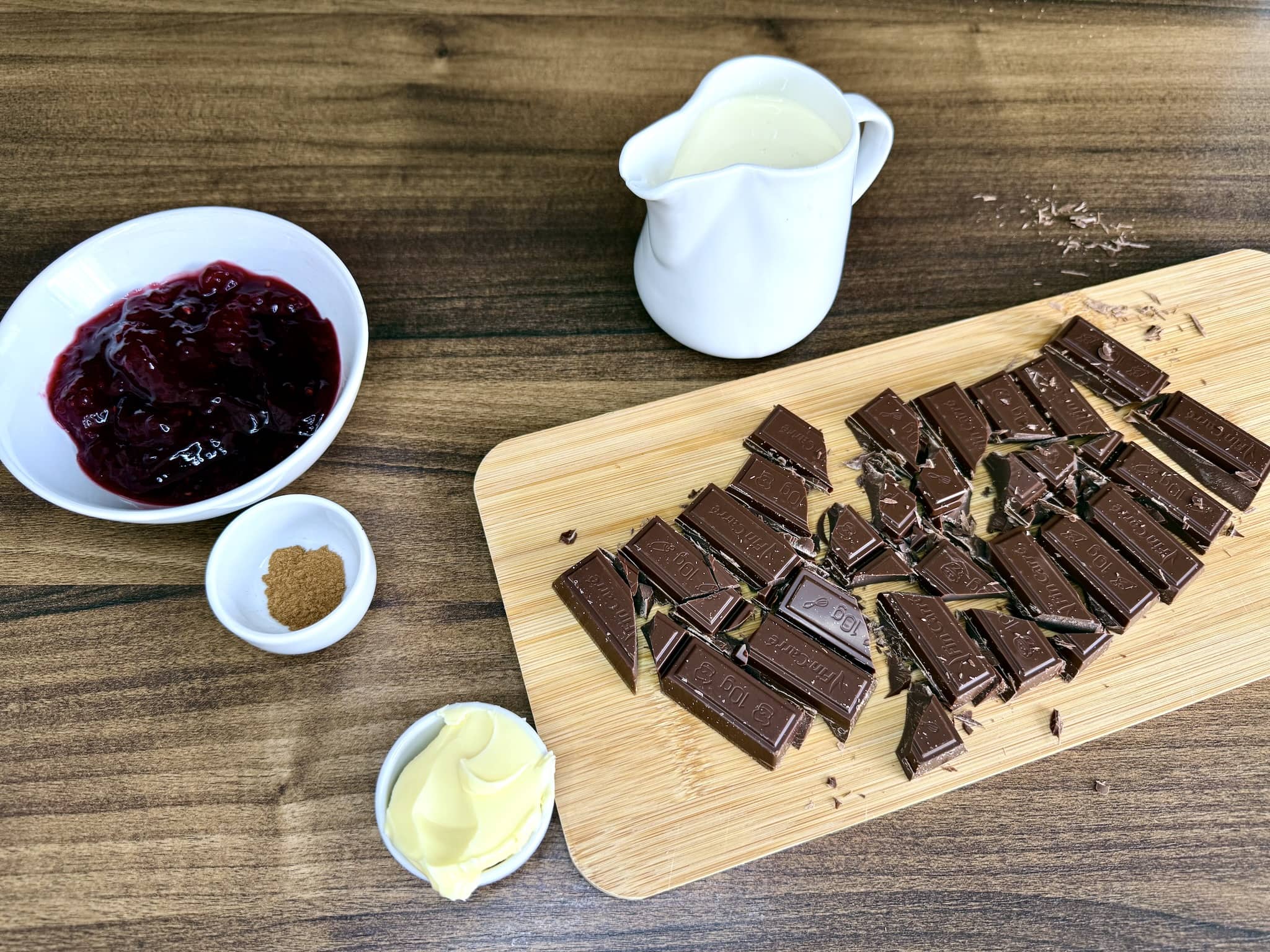 Jam, cinnamon, butter, and double cream on tabletop with chopped chocolate on a chopping board