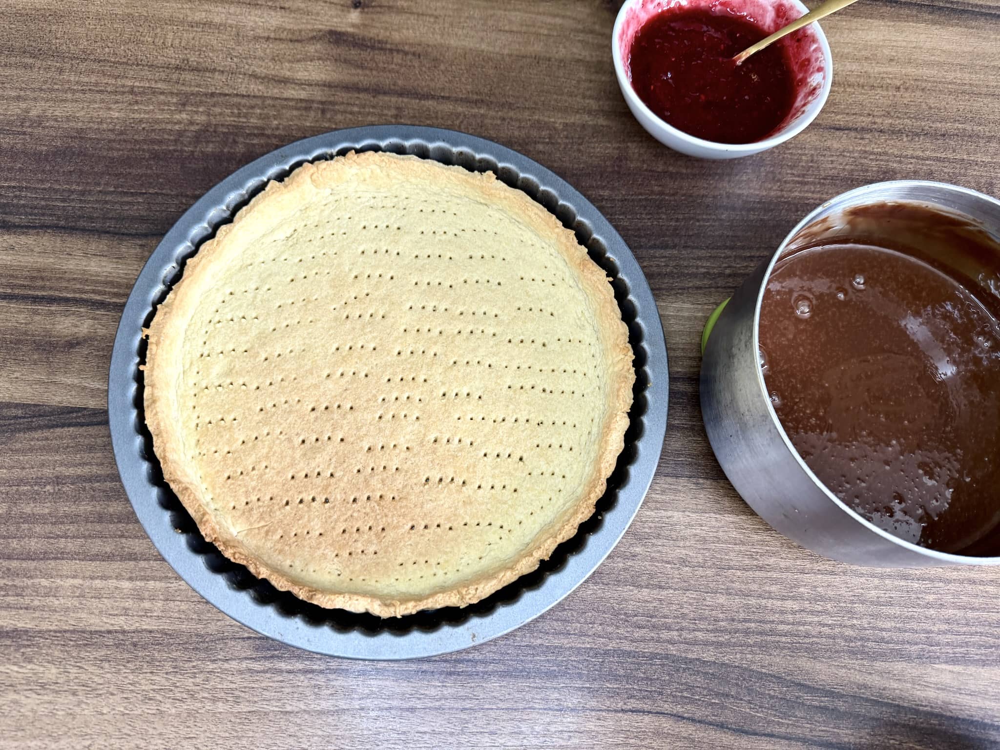 Tart nicely baked, still in the tin, with jam on the side and chocolate mix in a pan, all on tabletop
