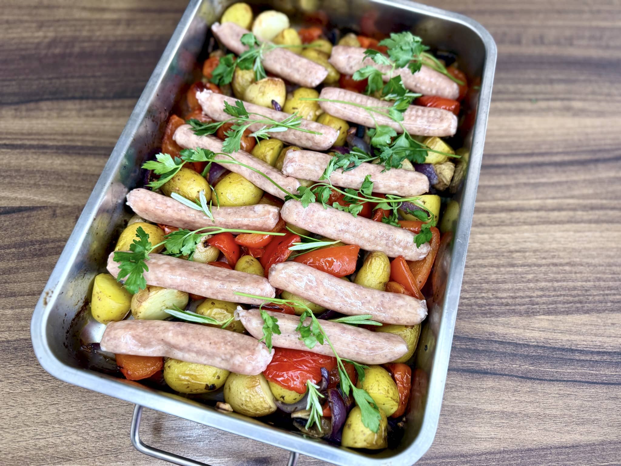 Fresh chipolata sausages placed on top of the roasted vegetables