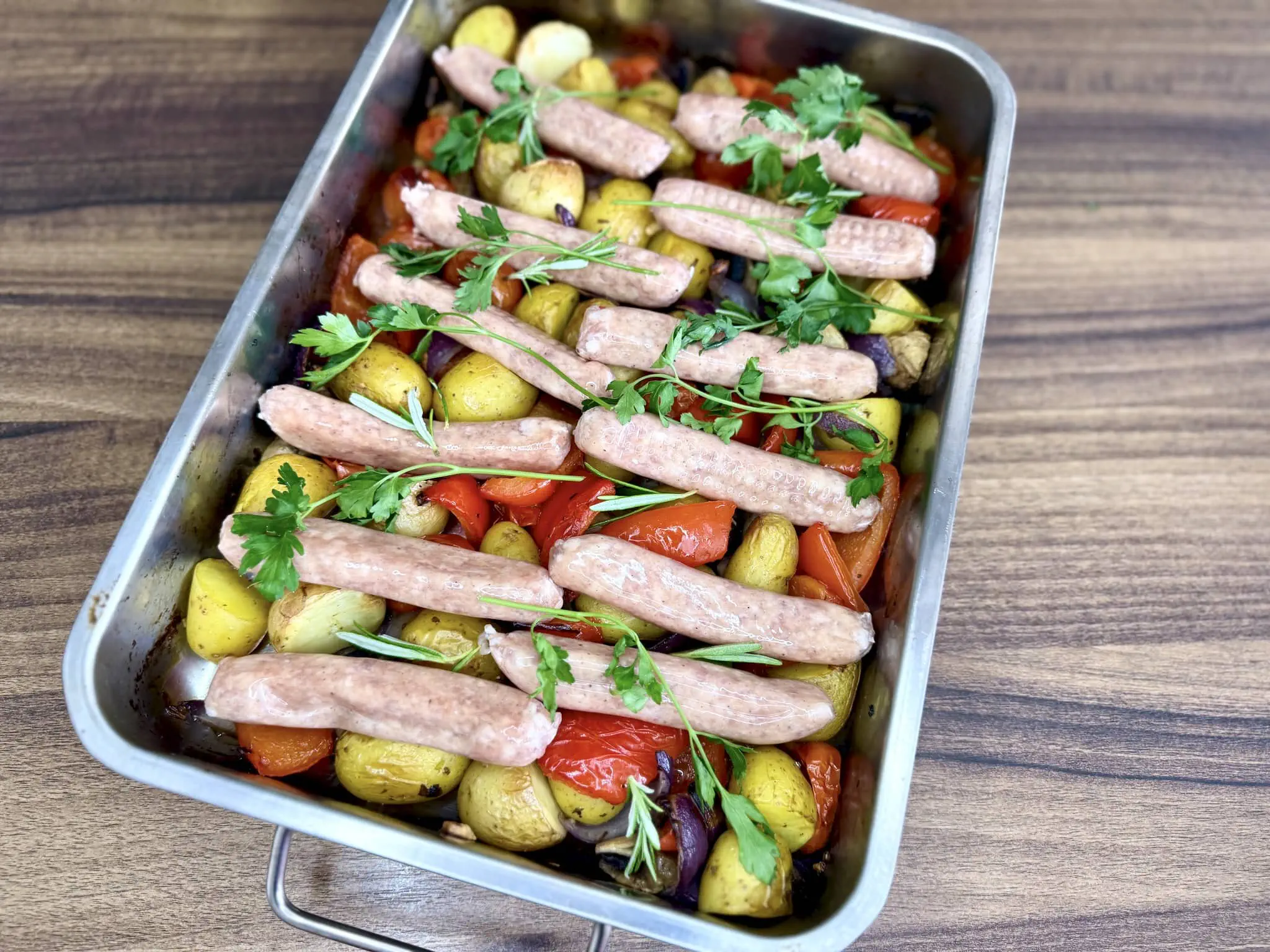Świeże kiełbaski chipolata ułożone na pieczonych warzywach