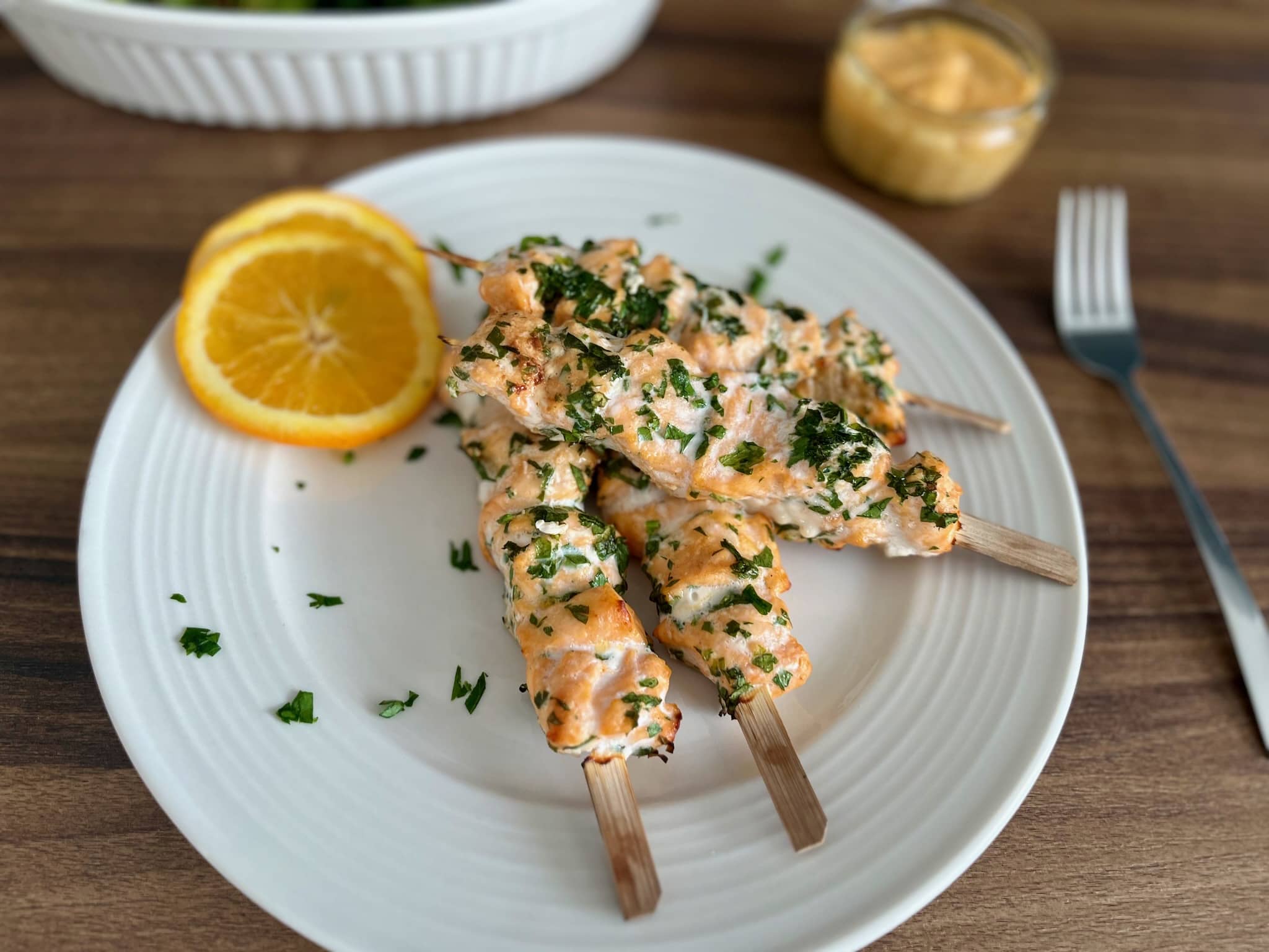 Nicely baked salmon skewers on a plate with orange slices on a side